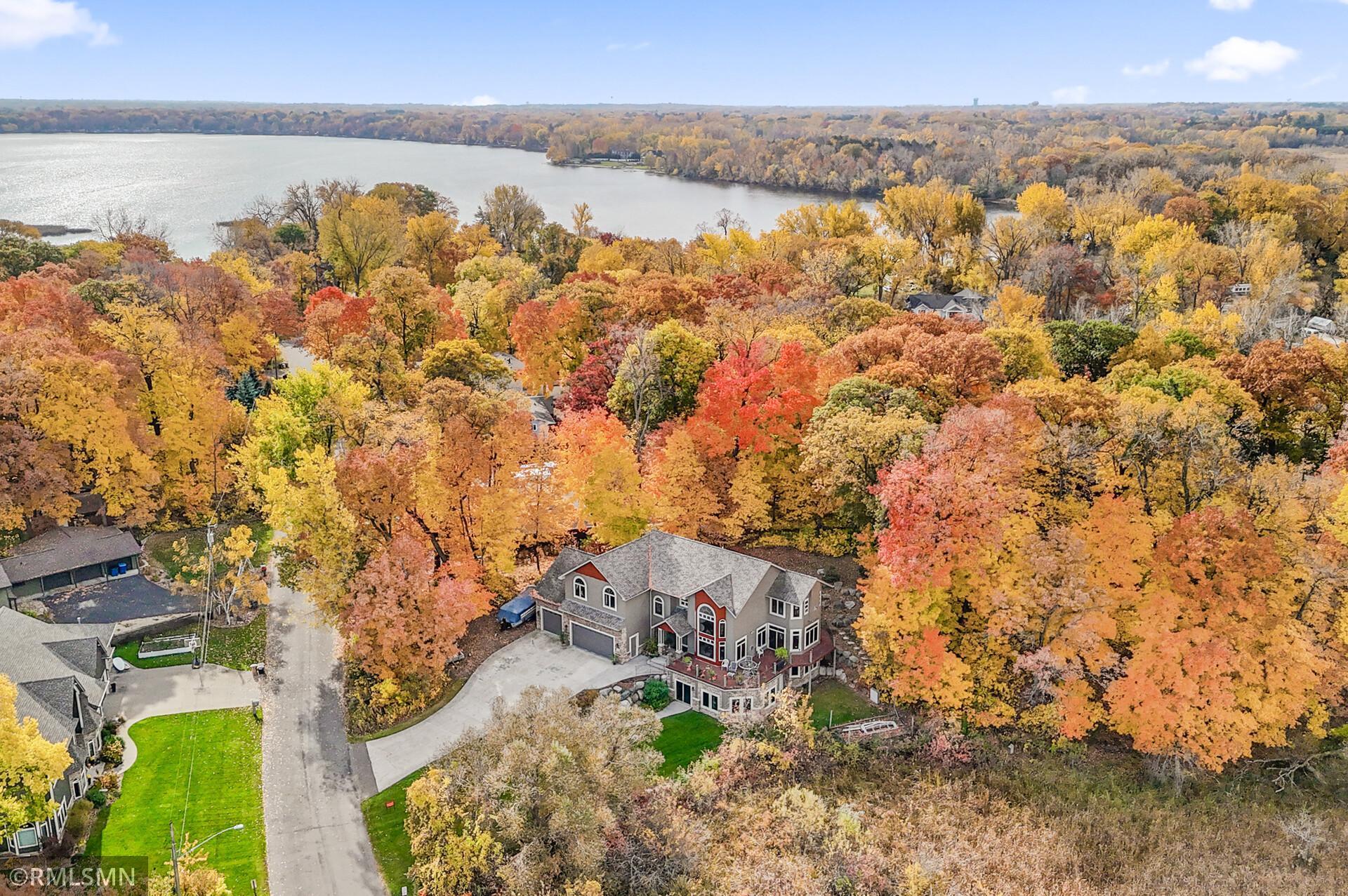 Aerial view of a multi-level home among colorful autumn trees, with a lake beyond.