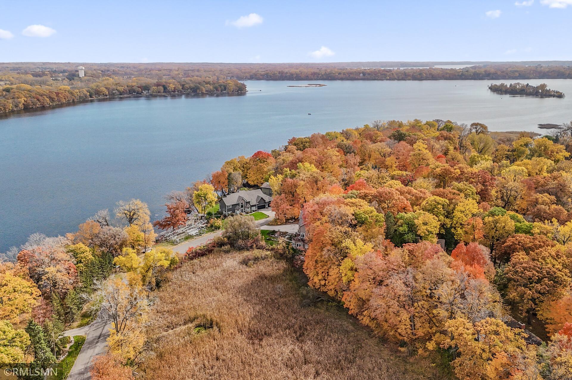 Aerial view of a lakeside home surrounded by colorful autumn trees beside a broad lake.