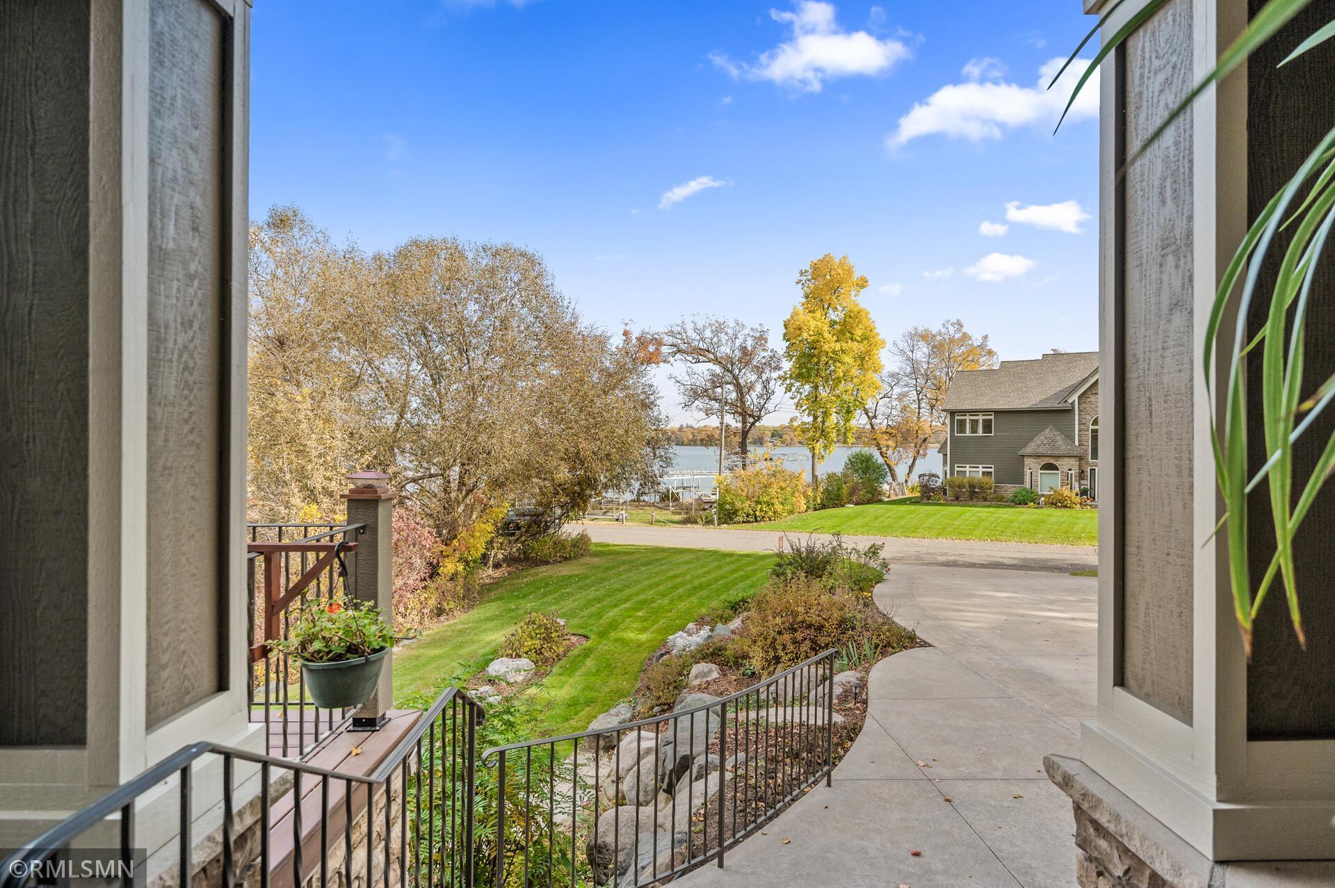 Entry walkway and landscaped lawn lead toward a lake, framed by autumn trees and a neighboring home.