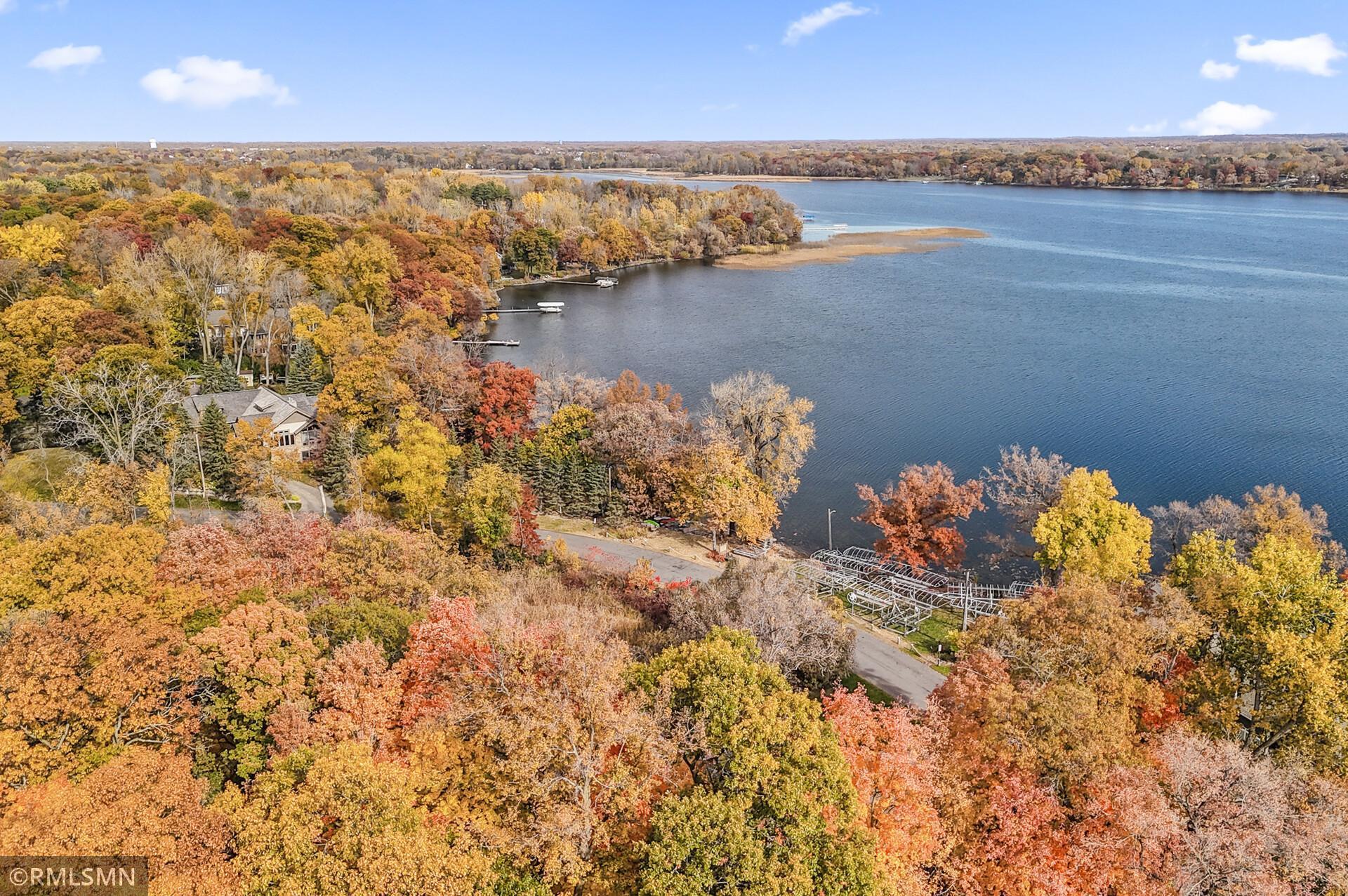 Aerial view of a lake and shoreline homes framed by vivid autumn foliage.