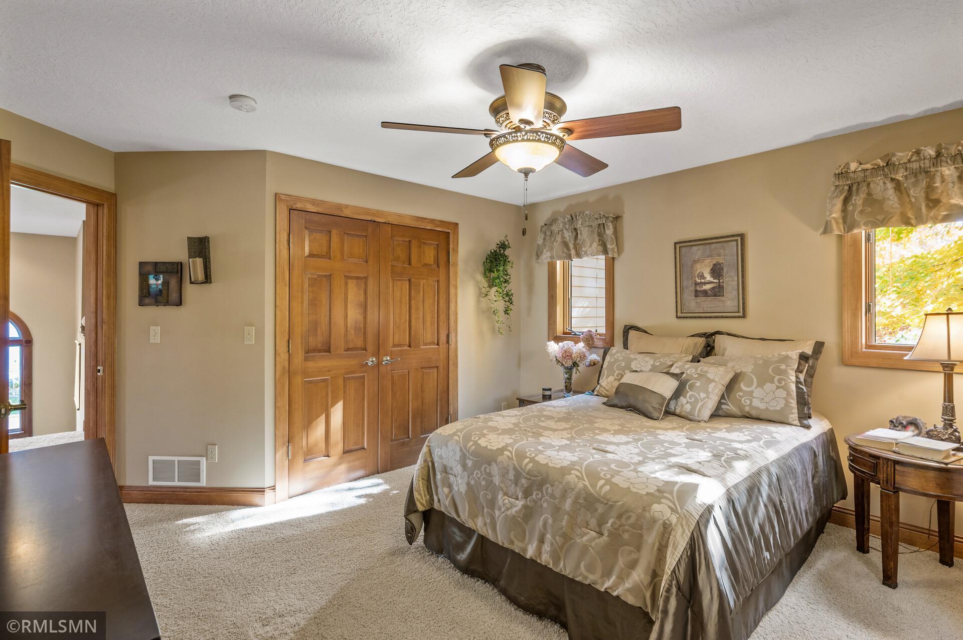 Furnished bedroom with a large floral-bedding bed, wood closet doors, and a ceiling fan.