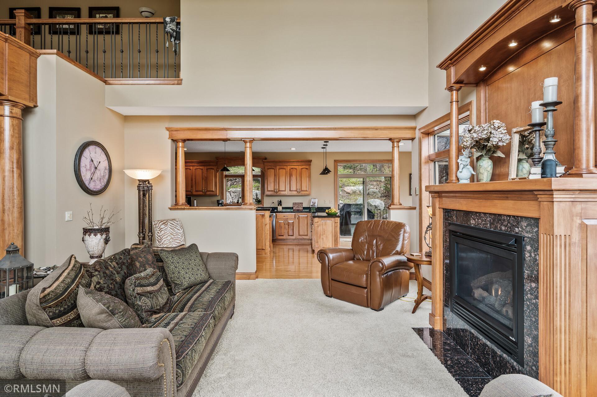 Living room with a large wood-trimmed fireplace, carpeted seating area, and open kitchen.