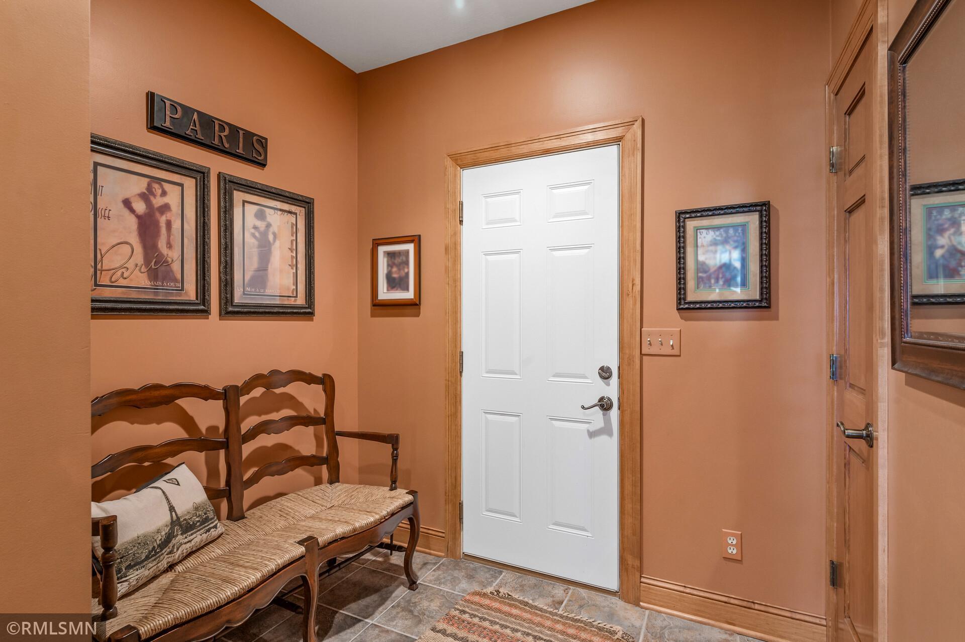 Entry hall with a wooden bench, Paris-themed art, terracotta walls, and a white paneled door.