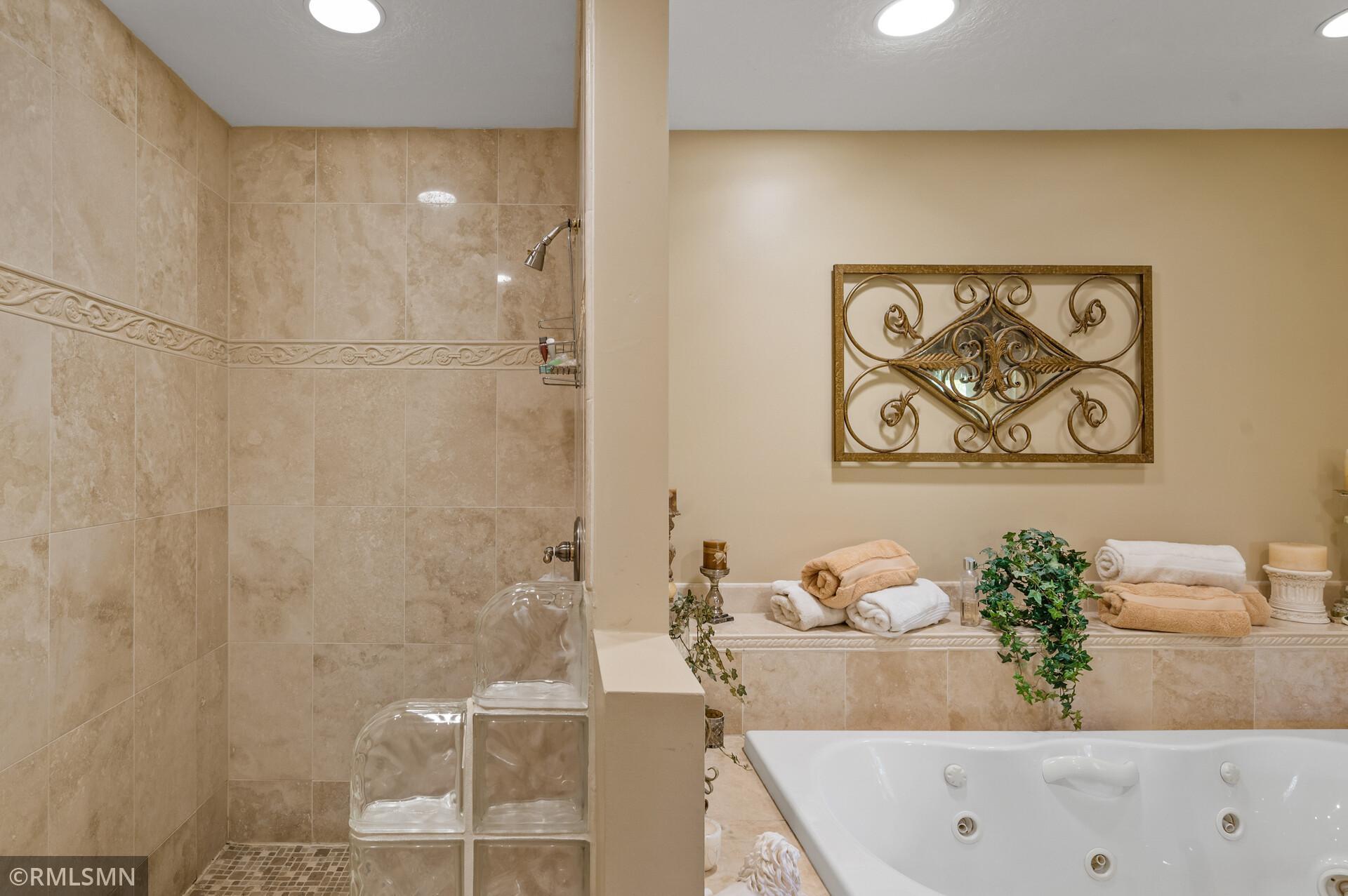 Bathroom with a tiled shower, glass-block partition, and white jetted bathtub.