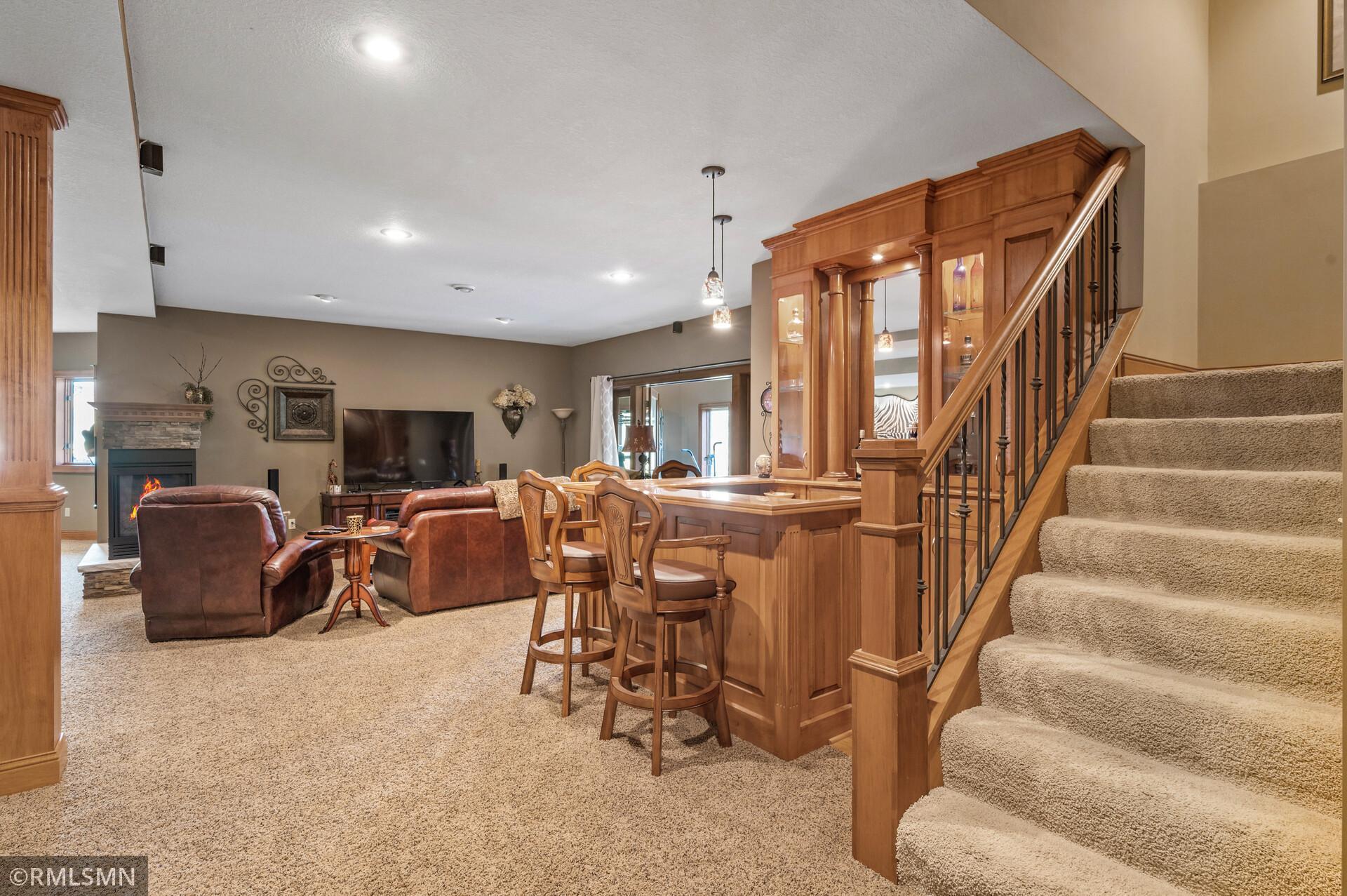 Family room with a built-in wooden bar, fireplace, leather seating, and carpeted staircase.