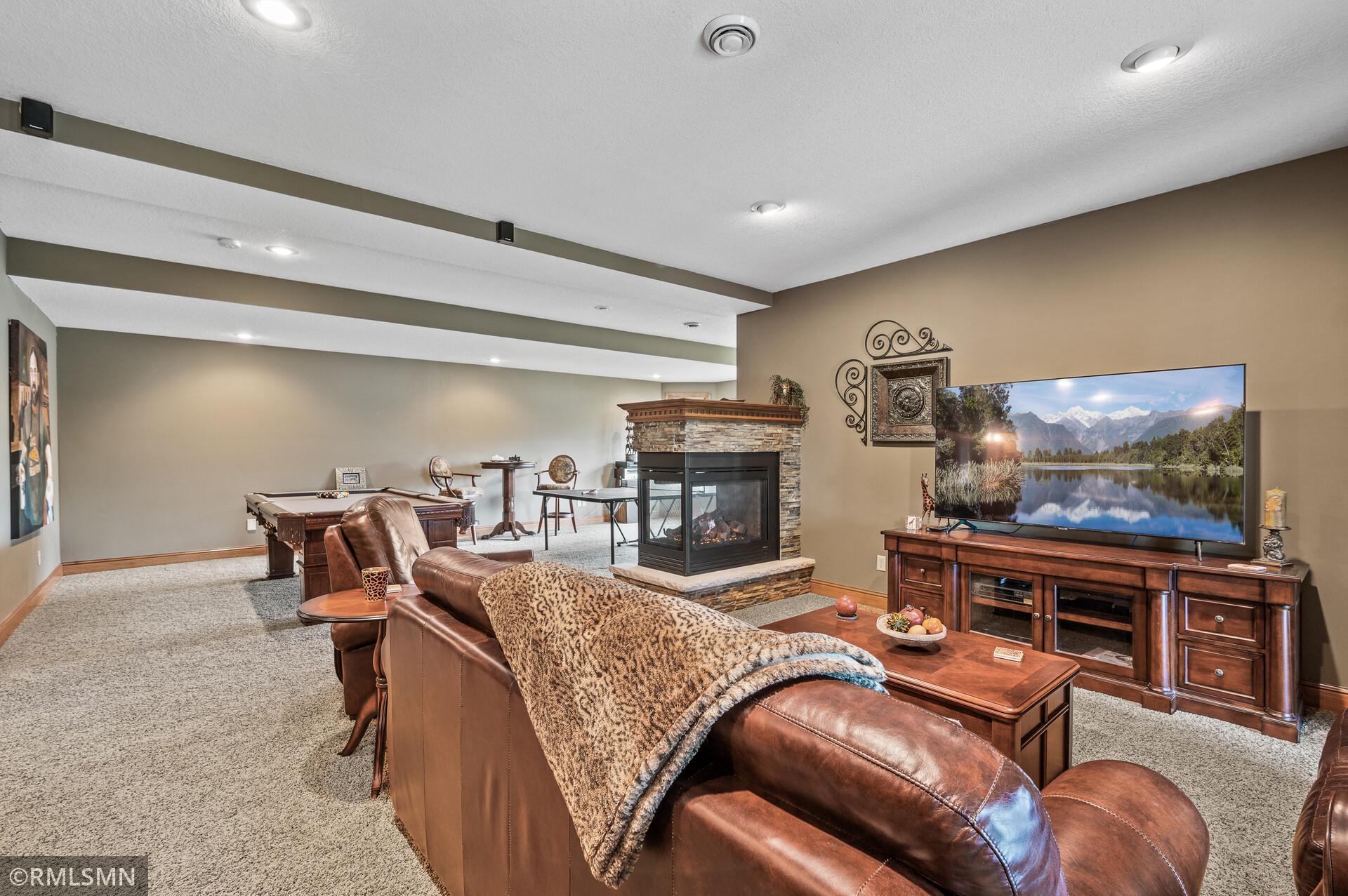 Furnished recreation room with a stone fireplace, pool table, and leather seating.