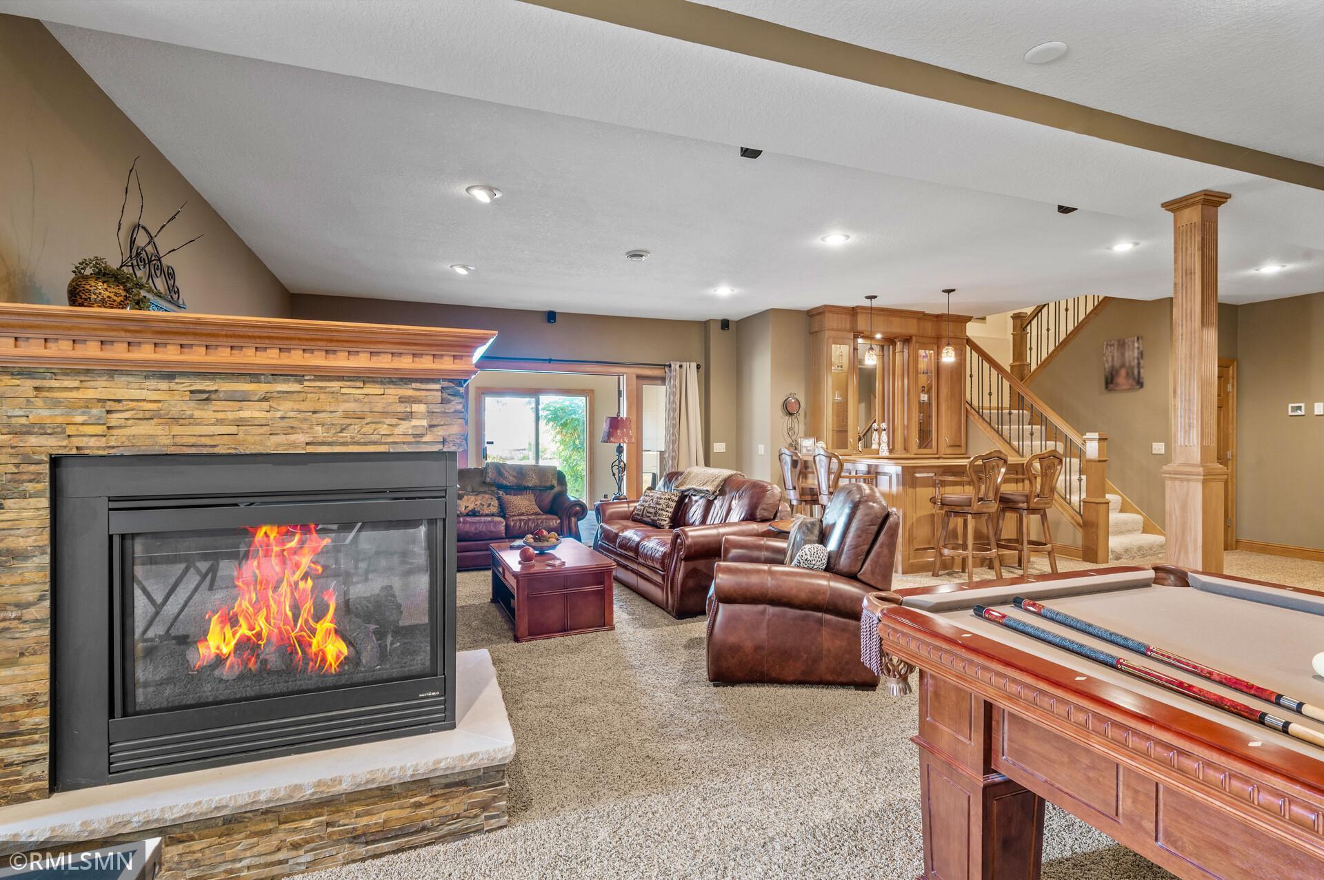 Recreation room with a stone fireplace, leather seating, pool table, and built-in wooden cabinetry.