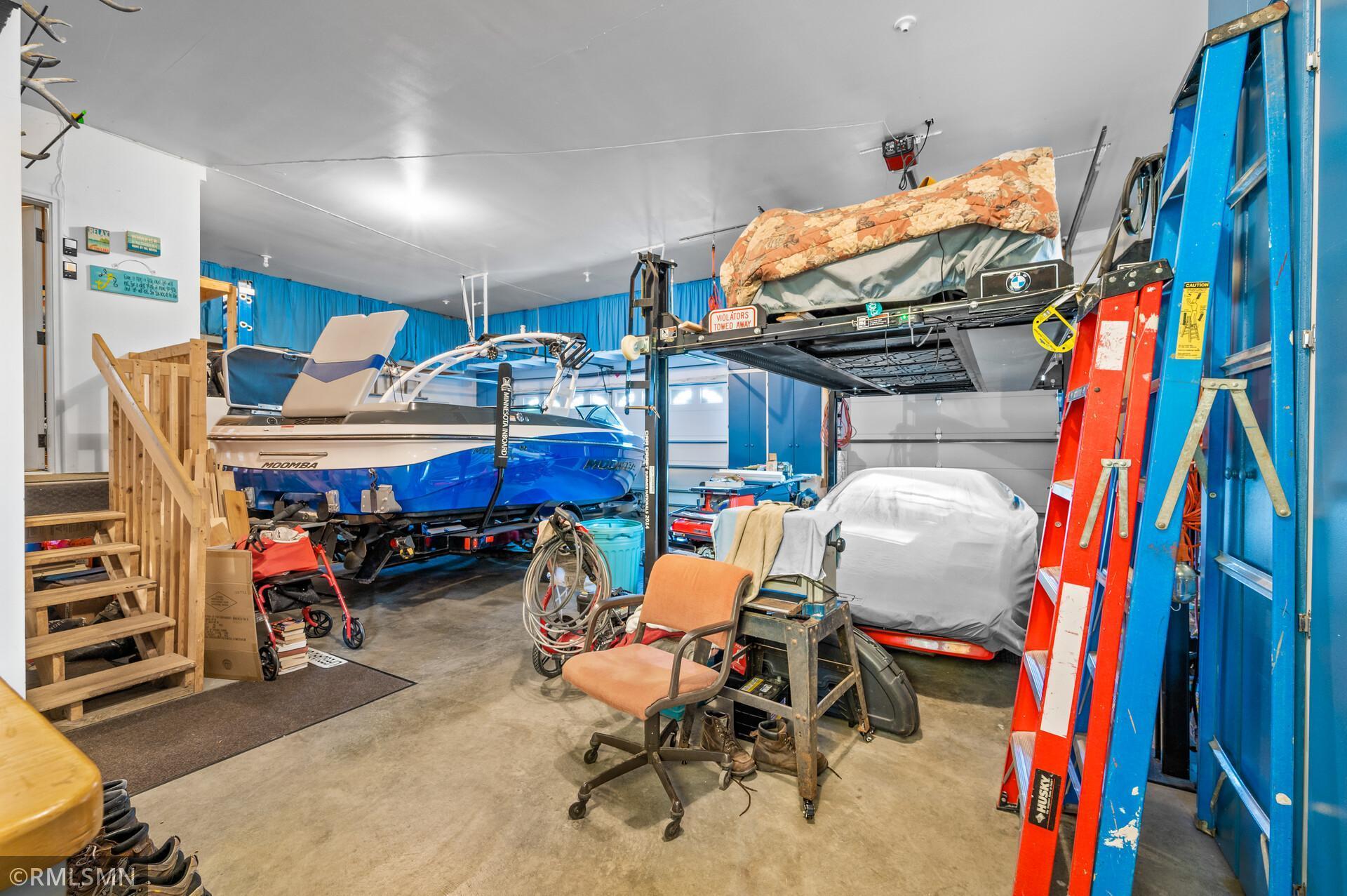 Garage with a blue boat, an overhead vehicle lift, and a covered vehicle.