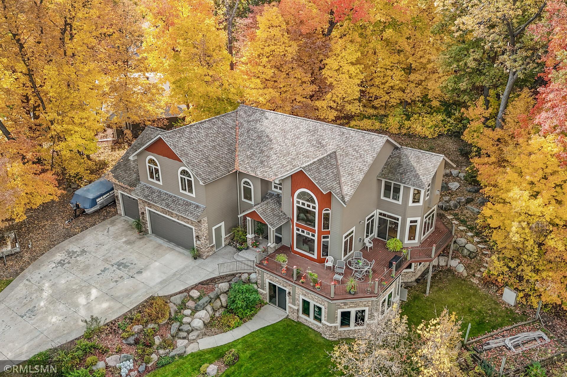 Aerial view of a large gray home and raised deck surrounded by colorful autumn trees.