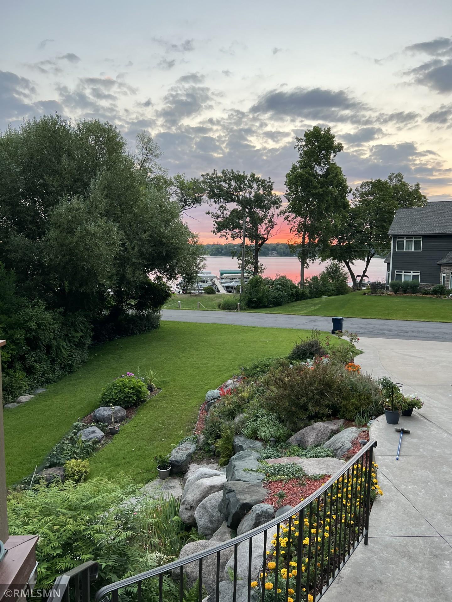 Landscaped yard overlooking a lake at sunset, with stone borders and flower beds beside the walkway.