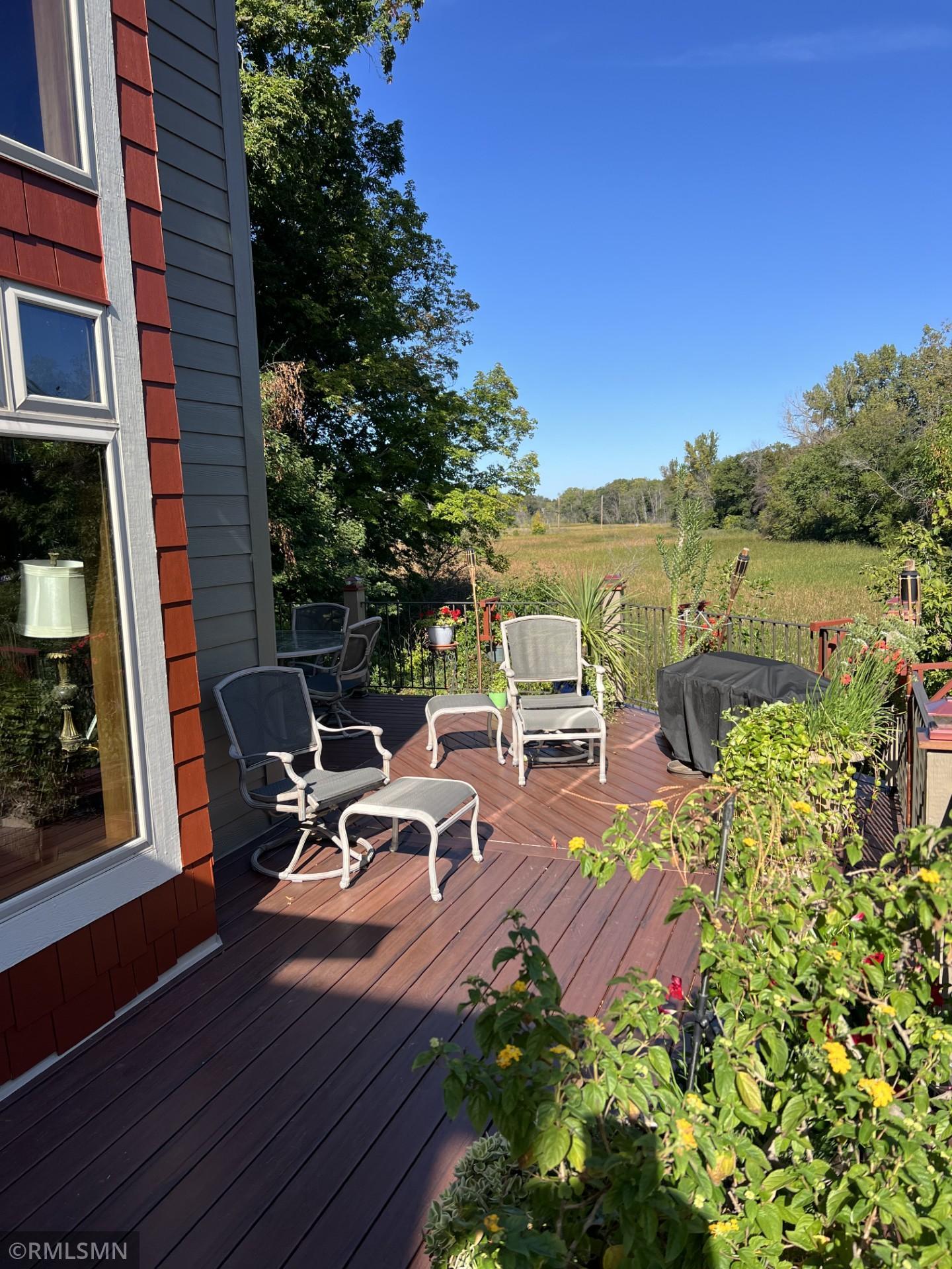 Furnished wood deck with patio seating, flowers, and an open meadow view.