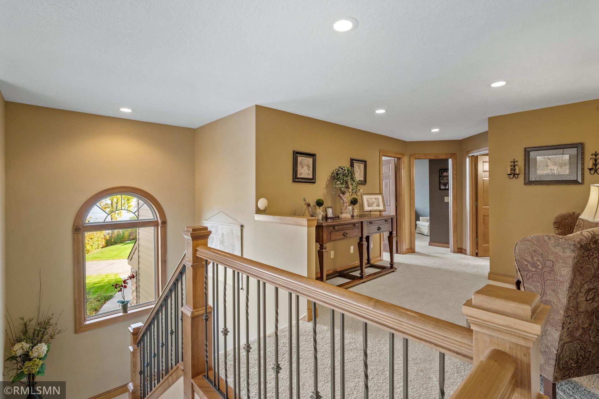 Upstairs landing overlooking a carpeted staircase, with an arched window and wood-and-metal railing.