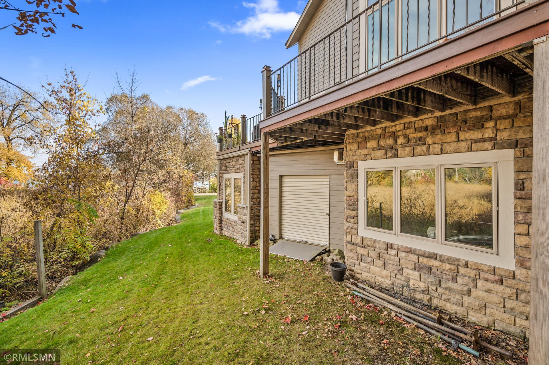 House rear with raised deck, stone siding, garage door, and autumn trees along the yard.