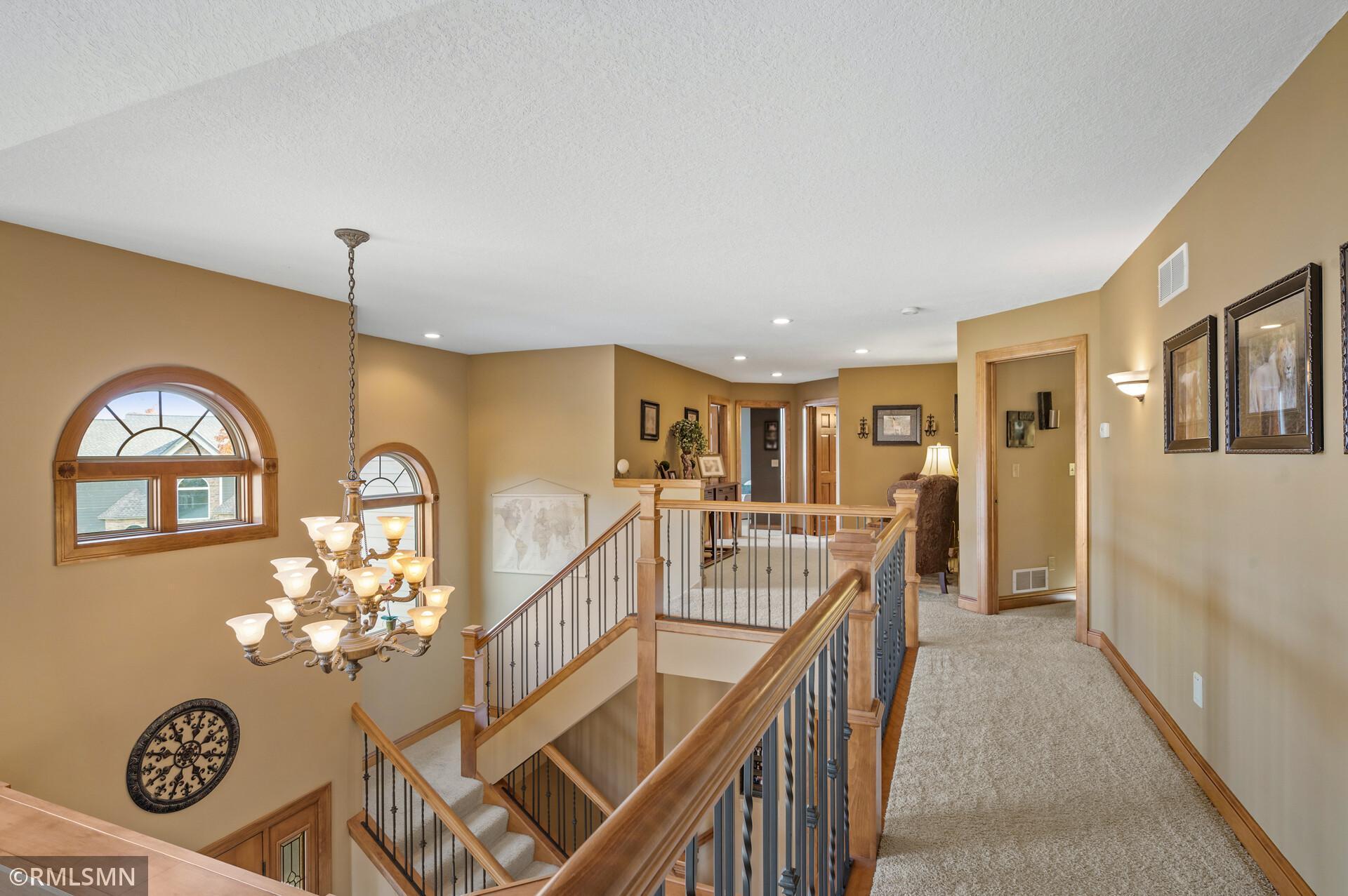 Upper-level landing overlooking a staircase, with wood railings, arched windows, and a chandelier.