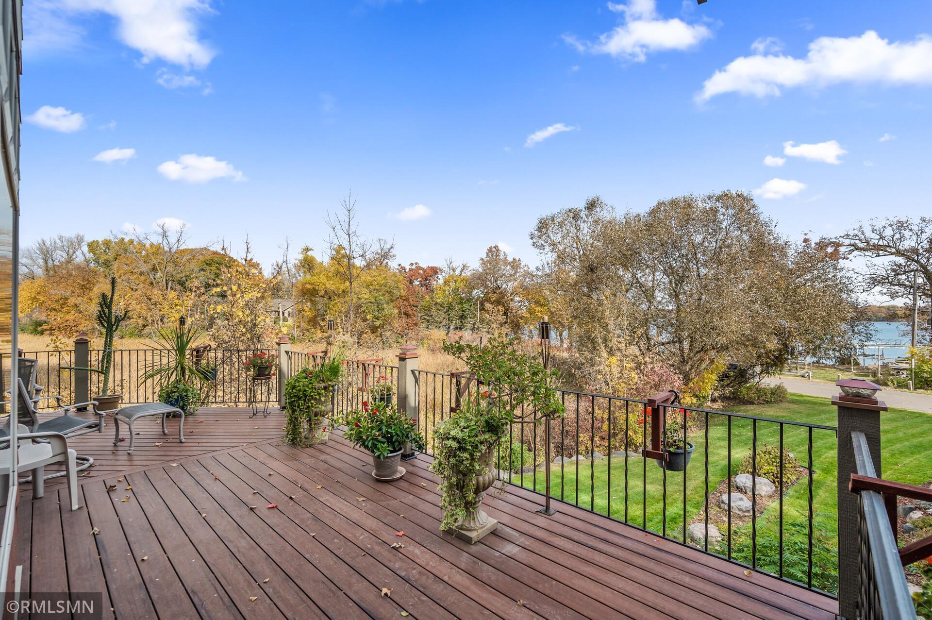 Wooden deck with patio seating and potted plants overlooking autumn trees and a lake.