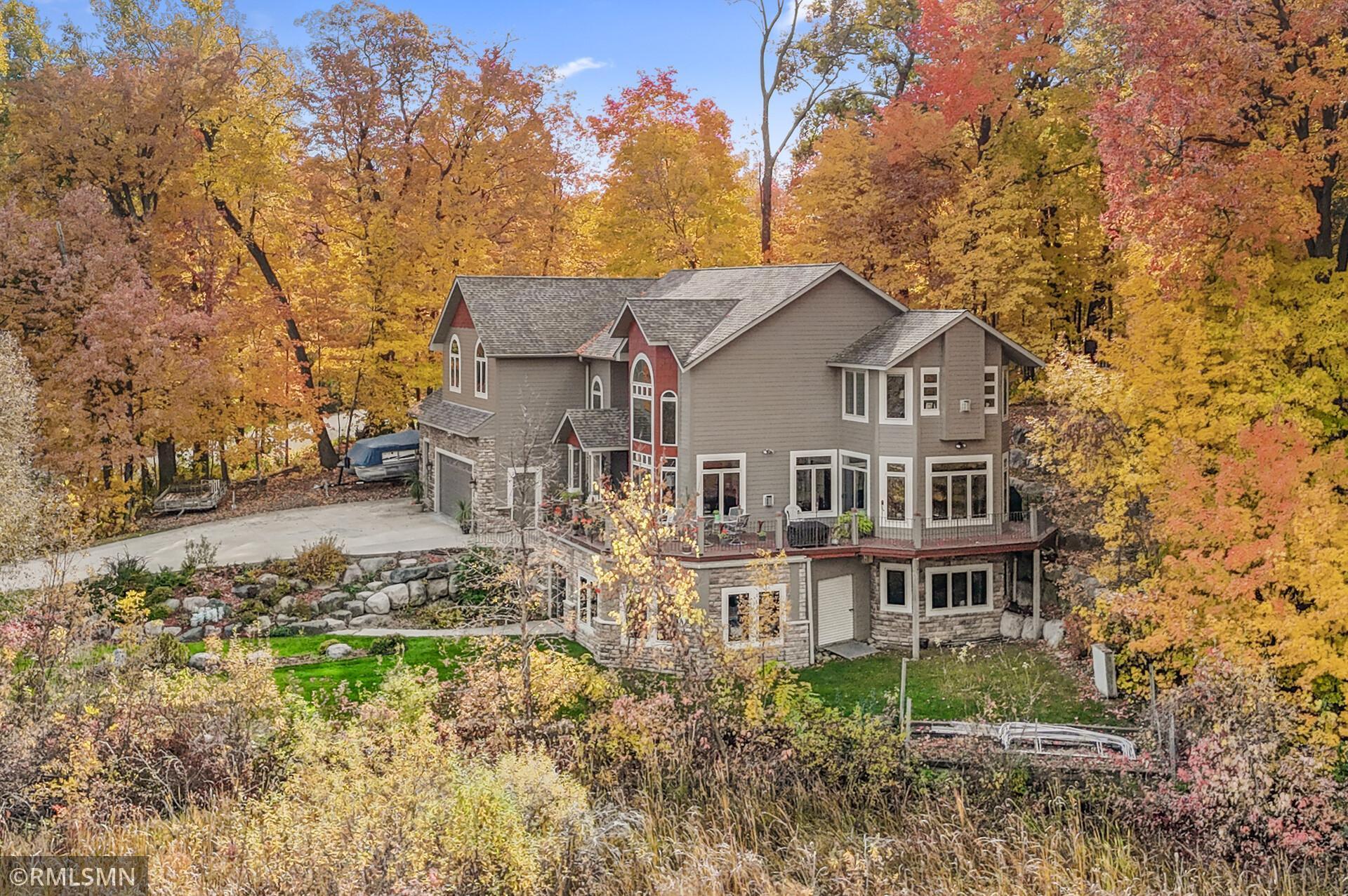 Large gray multi-level house with stone accents and a broad deck amid colorful autumn trees.