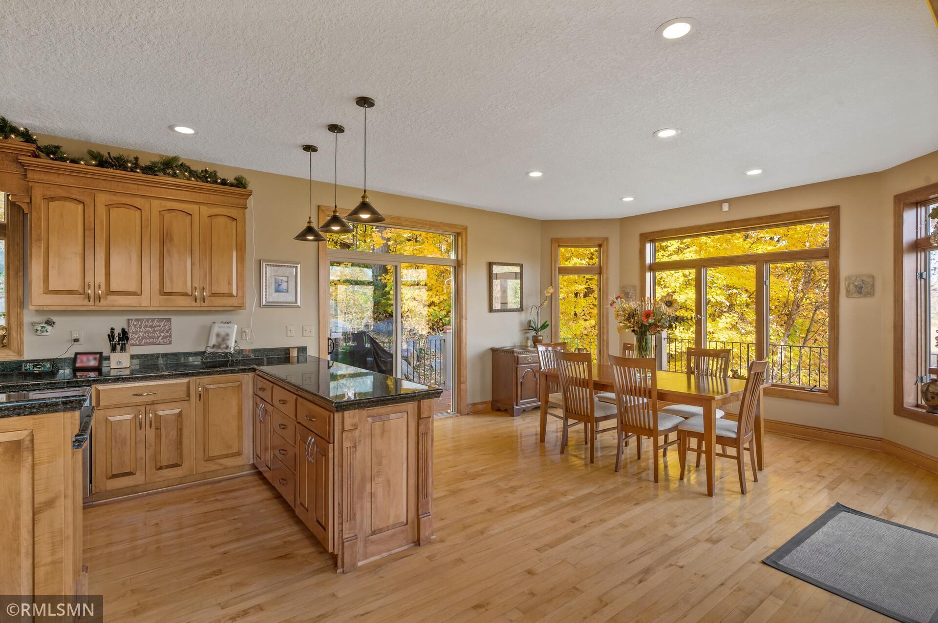 Kitchen and dining area with wood cabinetry, hardwood floors, and large windows overlooking autumn foliage.