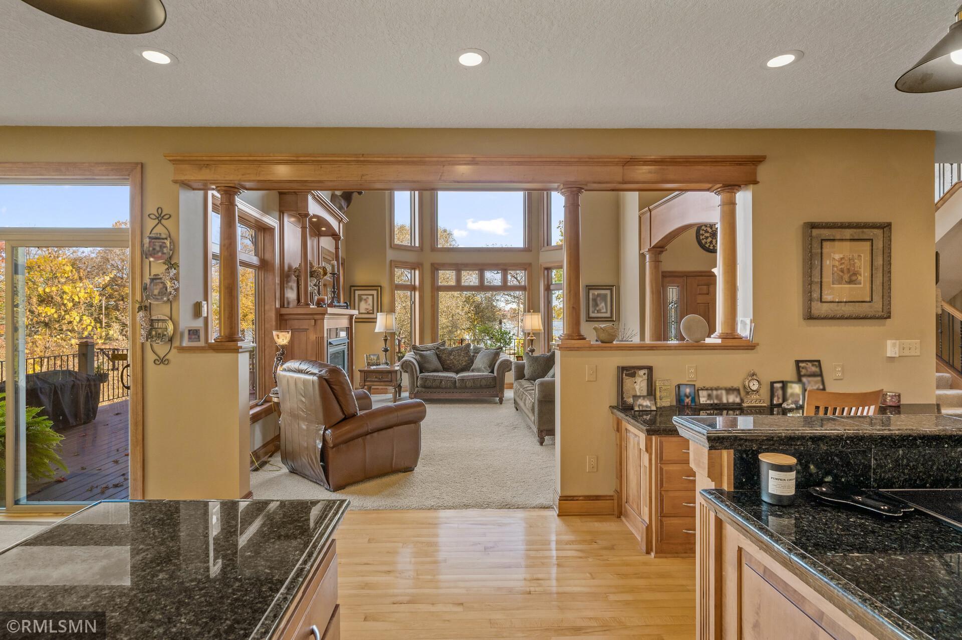 Kitchen with granite countertops opens to a vaulted living room with large windows overlooking water.