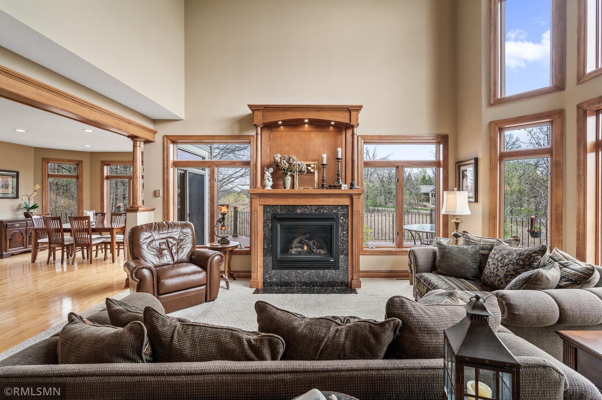 Living room with a tall wood-trimmed fireplace, expansive windows, and adjoining dining area.
