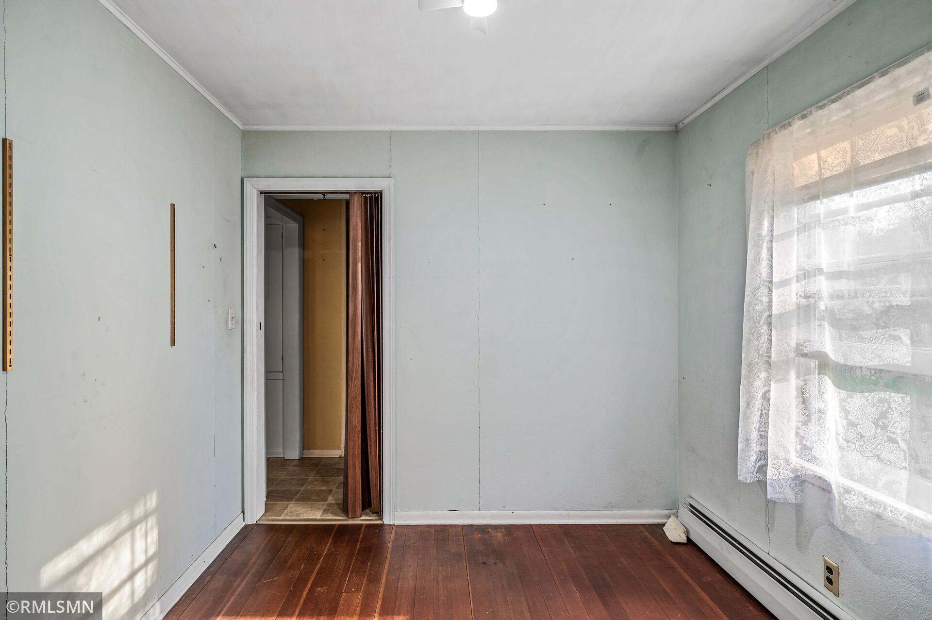 Empty room with pale green walls, dark hardwood floors, and a lace-curtained window.
