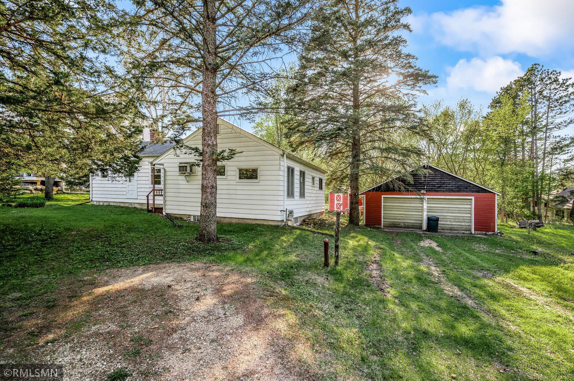 White house and red detached garage among mature trees, viewed across a gravel driveway.