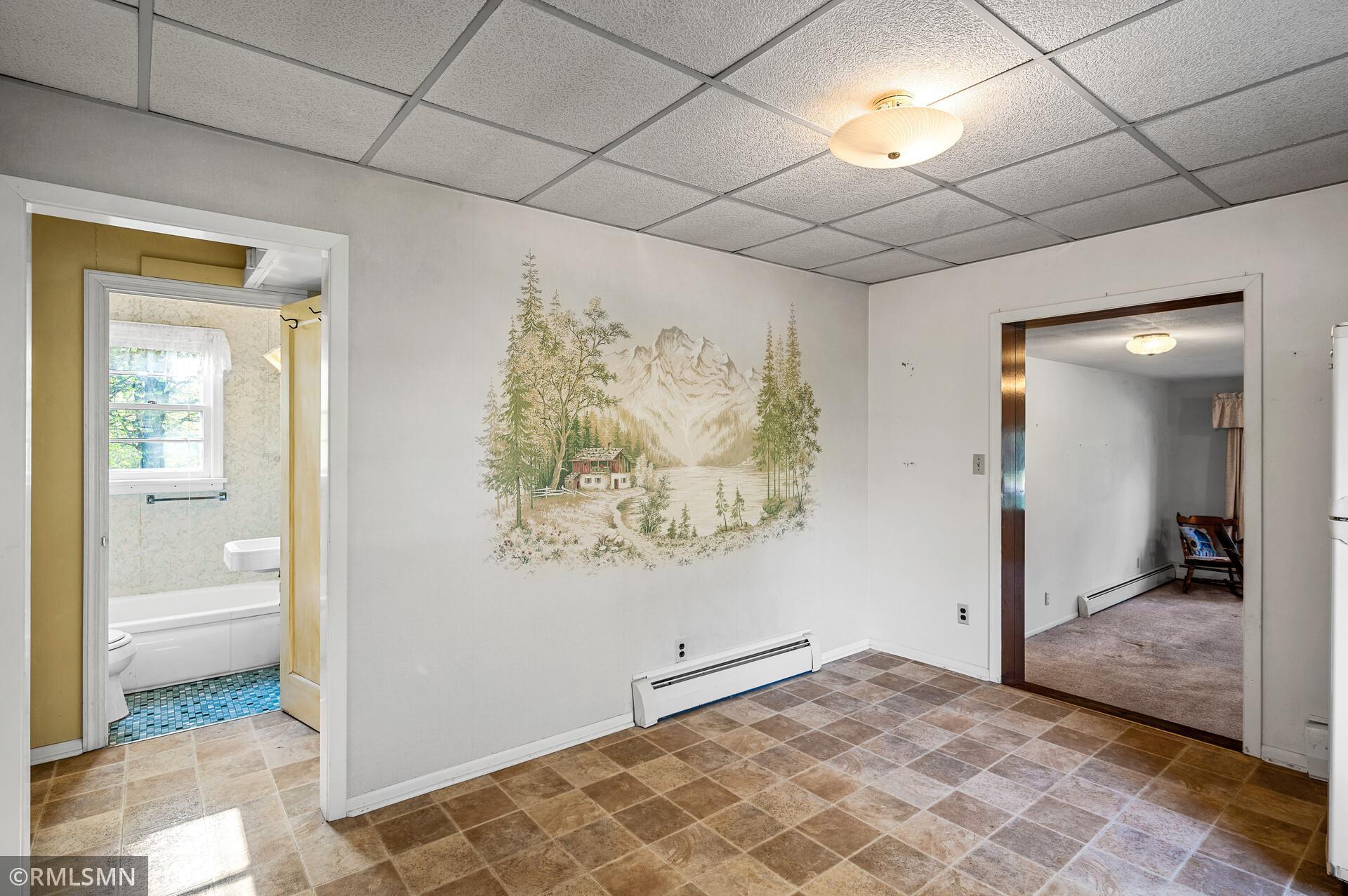 Tiled interior room with a mountain mural, bathroom doorway, and adjoining carpeted room.
