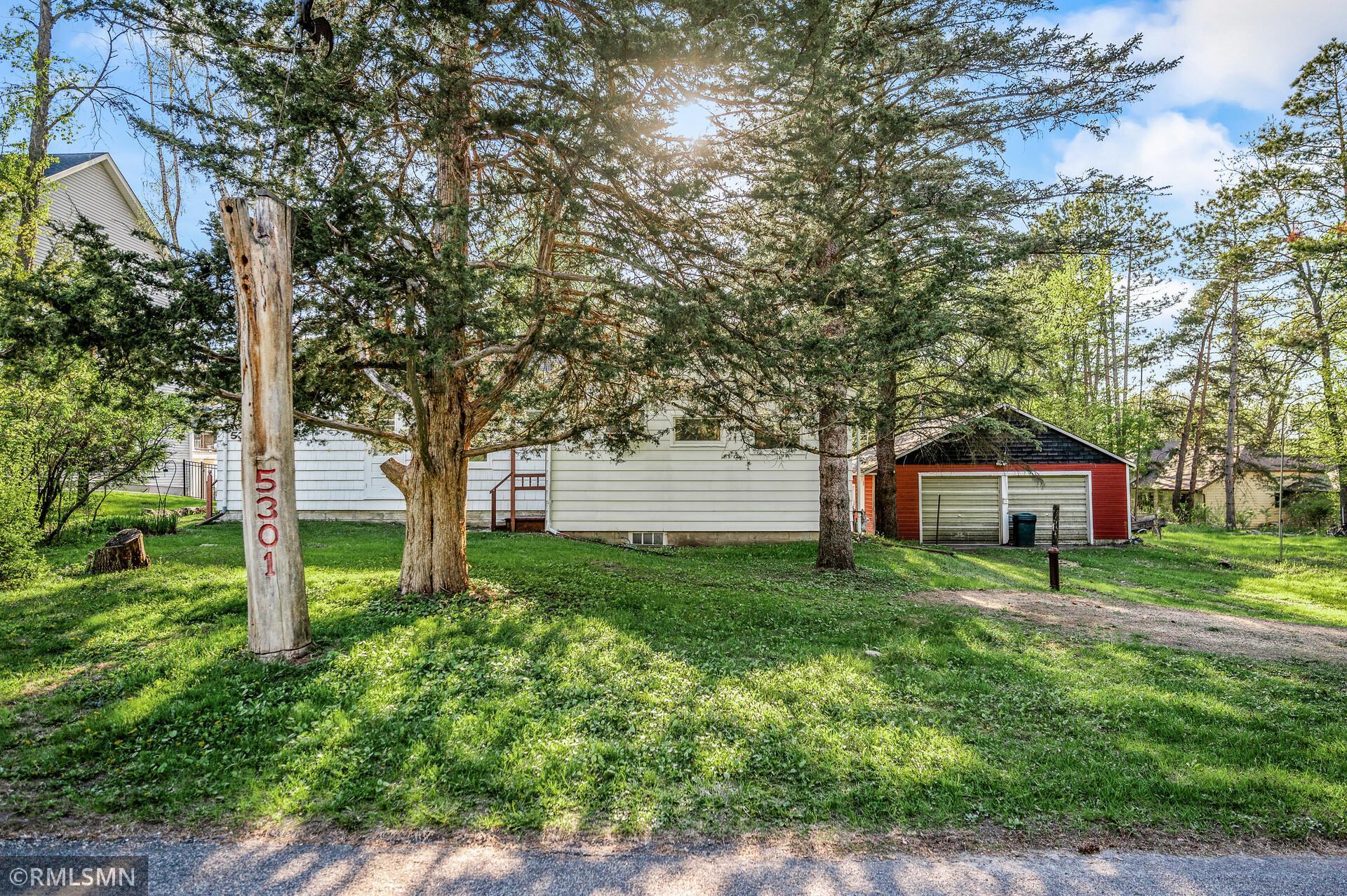 White house and red detached garage among mature trees, with address 5301 on a wooden post.