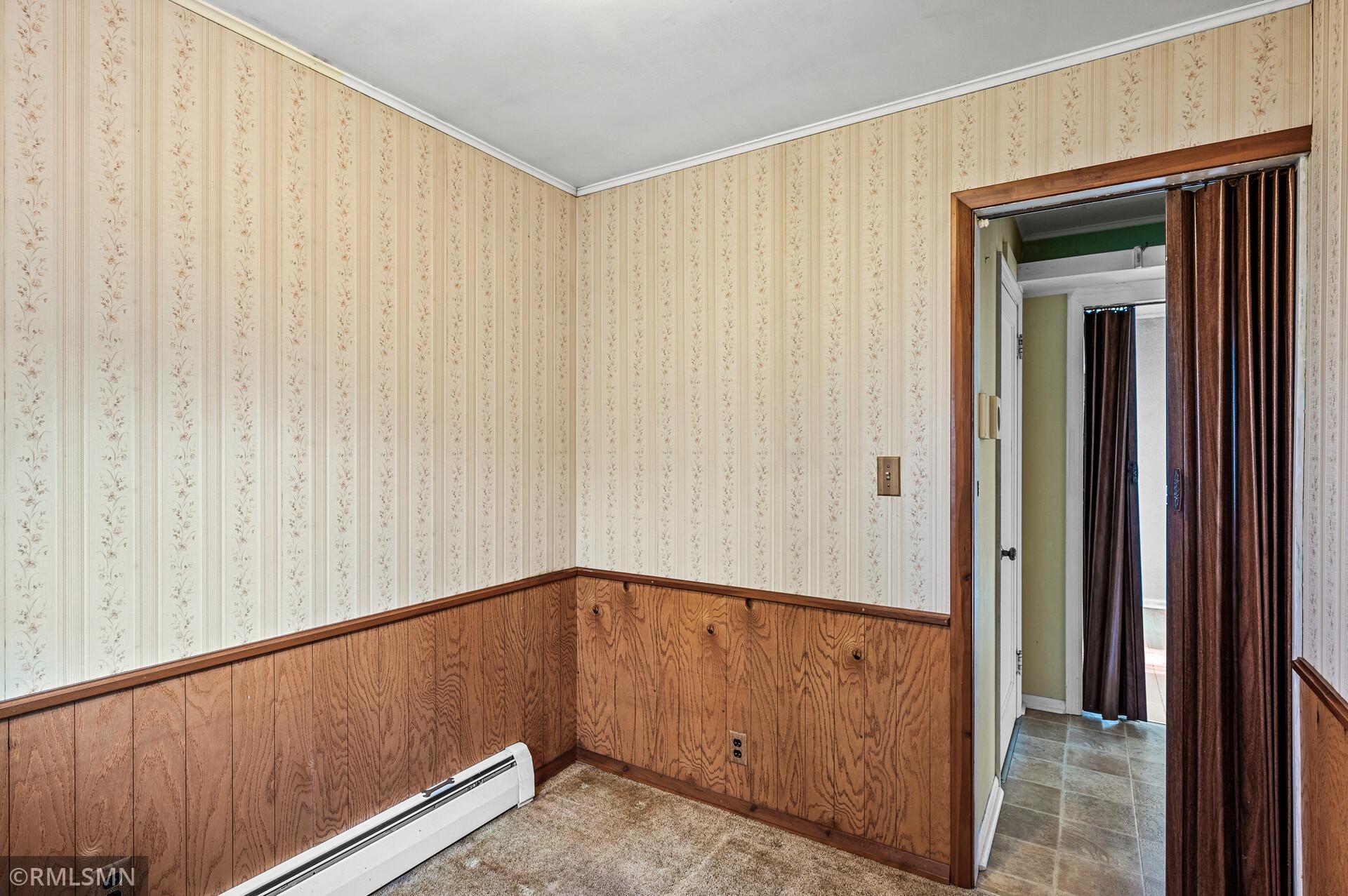 Unfurnished room with floral wallpaper, wood paneling, carpet, and a baseboard heater.