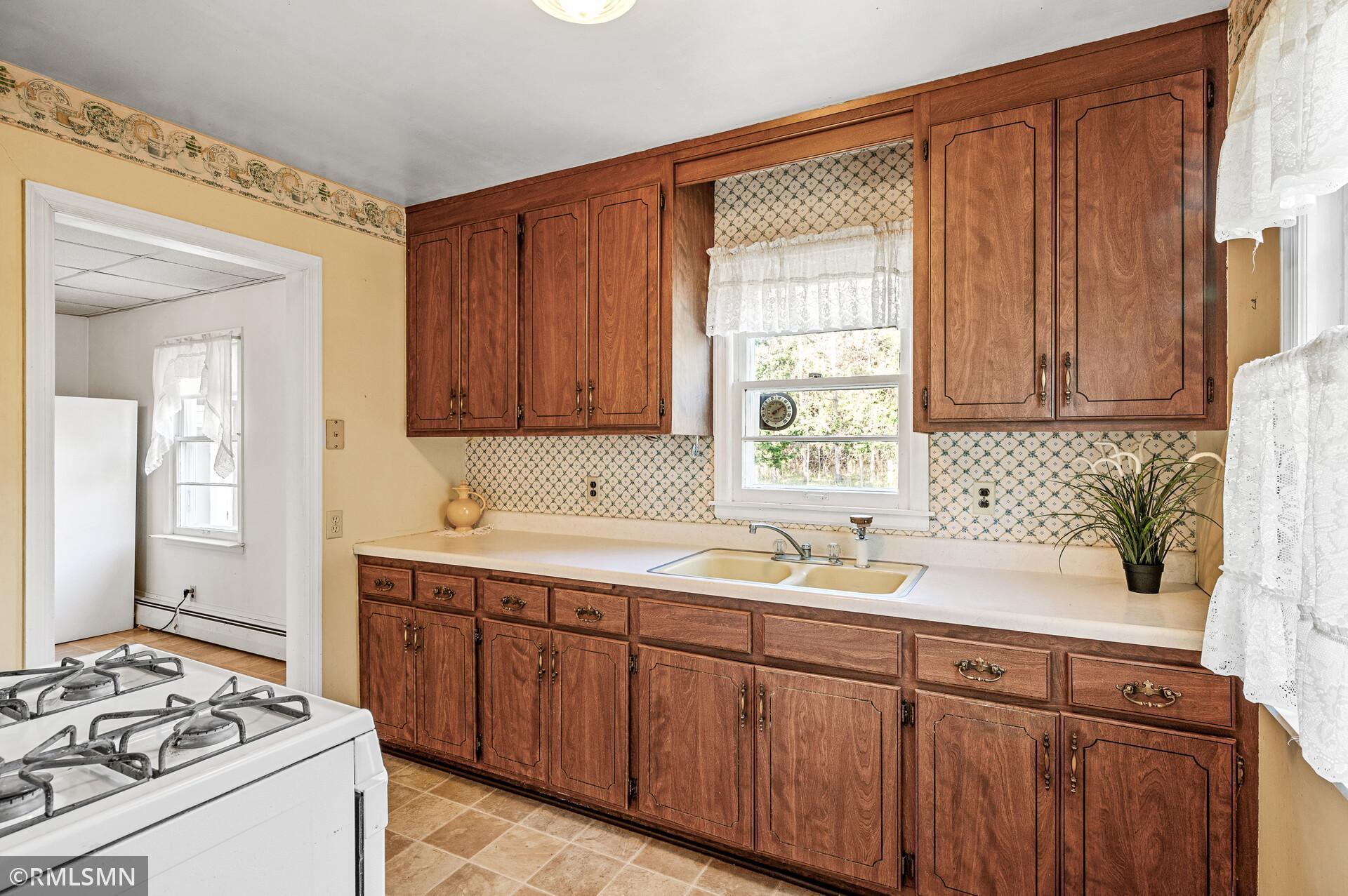 Kitchen with dark wood cabinets, patterned backsplash, and a double sink beneath the window.