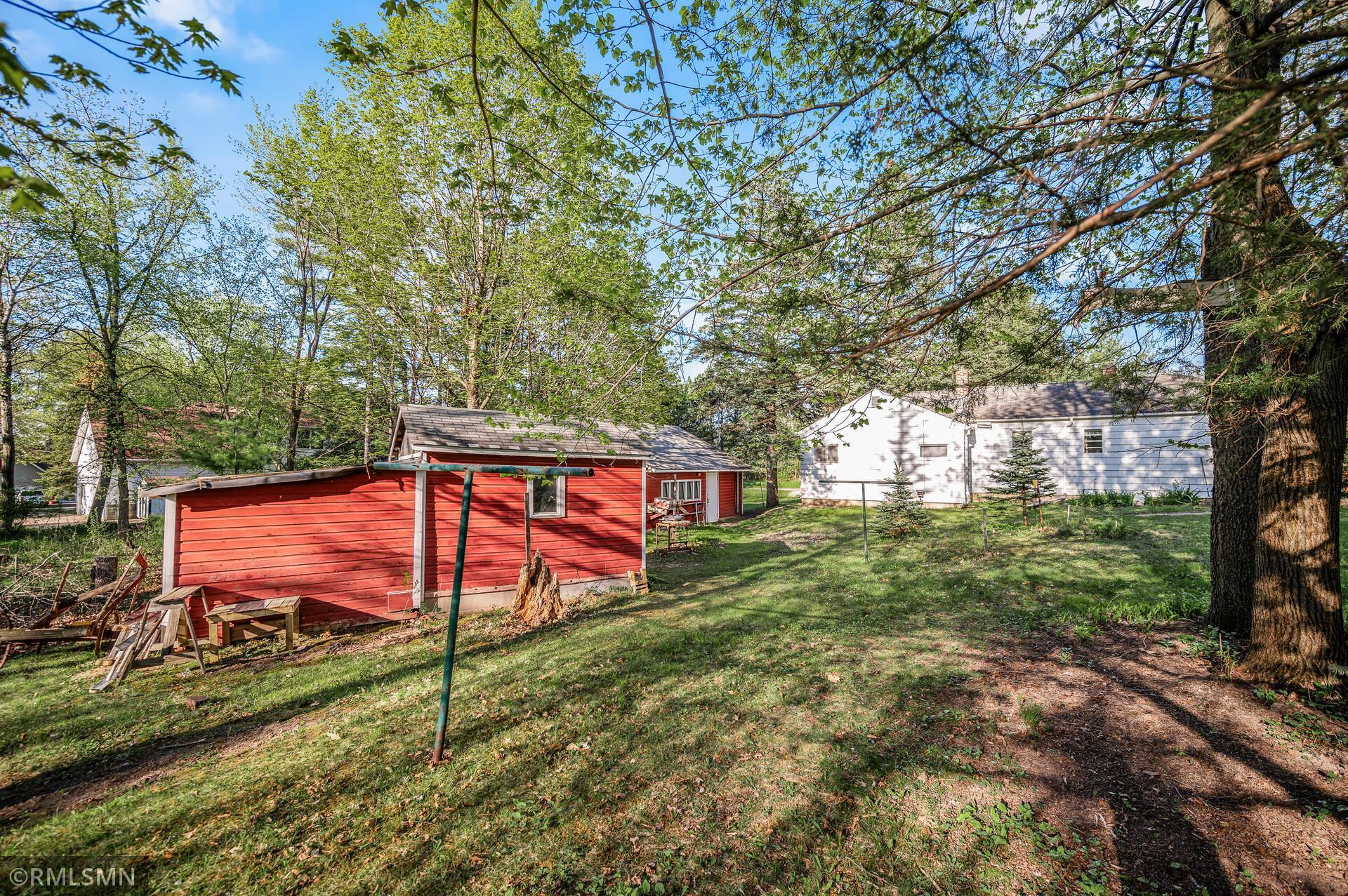 Backyard with a red detached outbuilding, white house, mature trees, and grassy lawn.