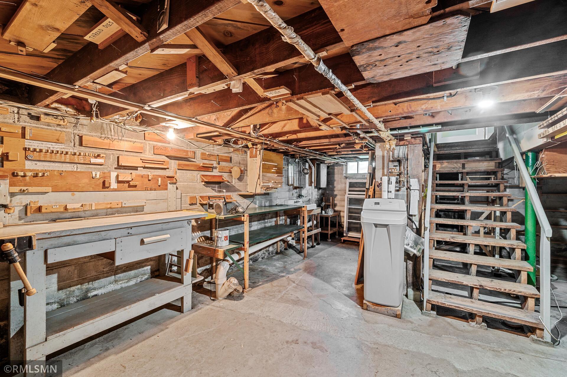 Basement workshop with extensive built-in workbenches and open wooden stairs.