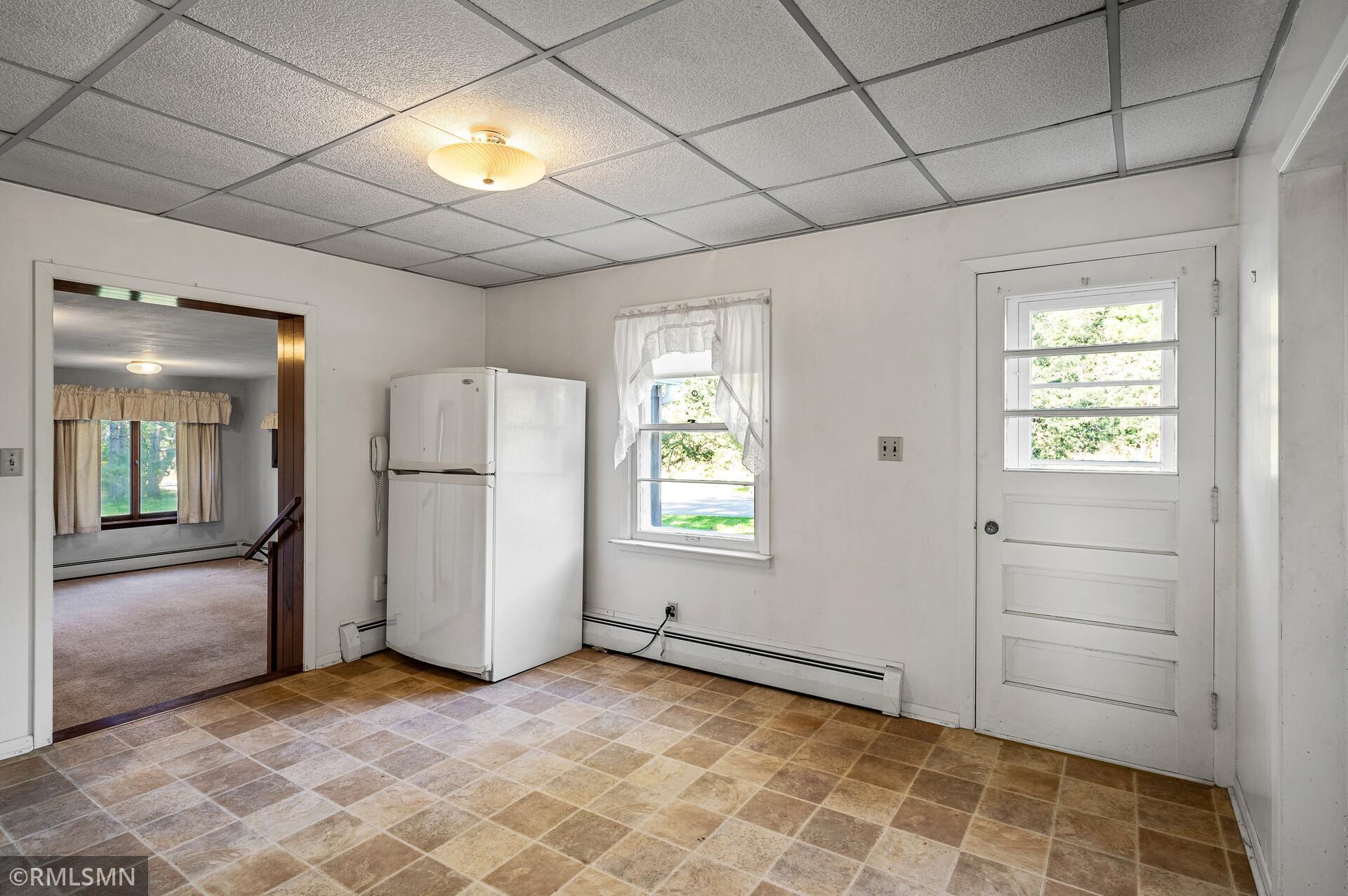 Mostly empty kitchen with tan tile flooring, a white refrigerator, and a windowed exterior door.