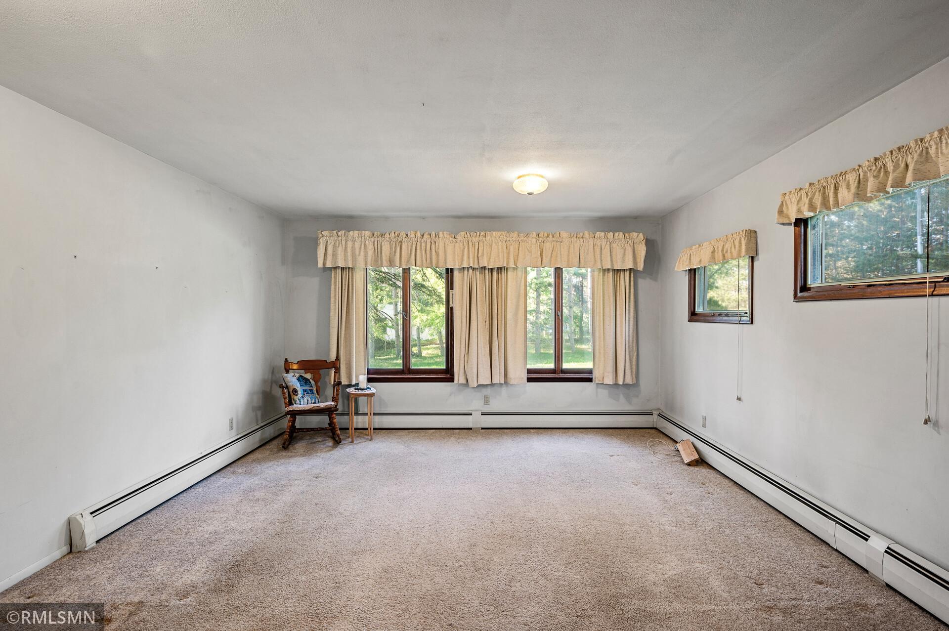 Carpeted room with wood-framed windows, beige curtains, and a wooden chair.