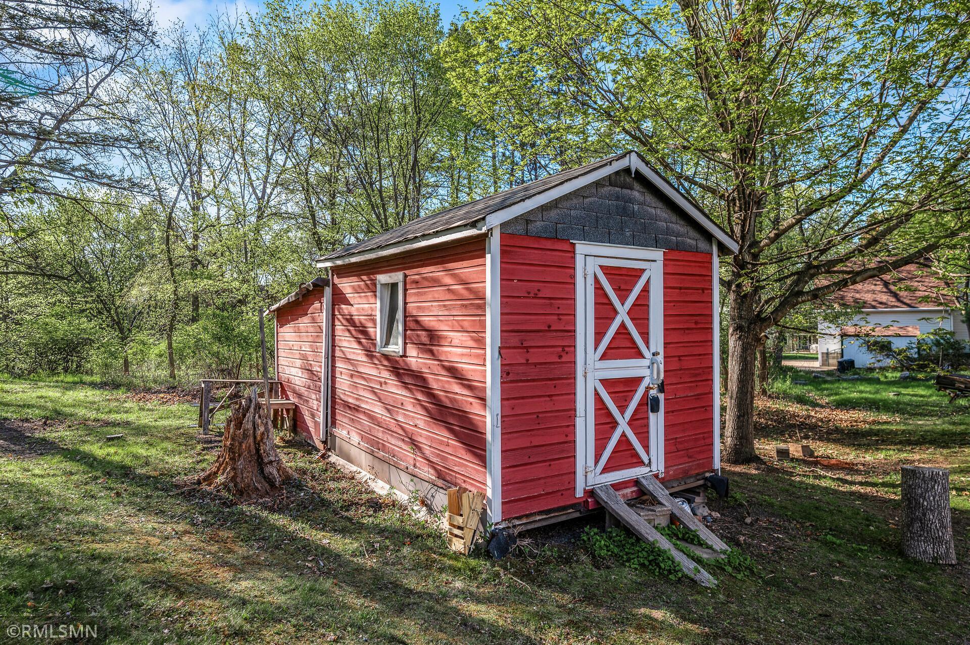 Red wooden shed with white trim and a crossbuck door in a leafy yard.
