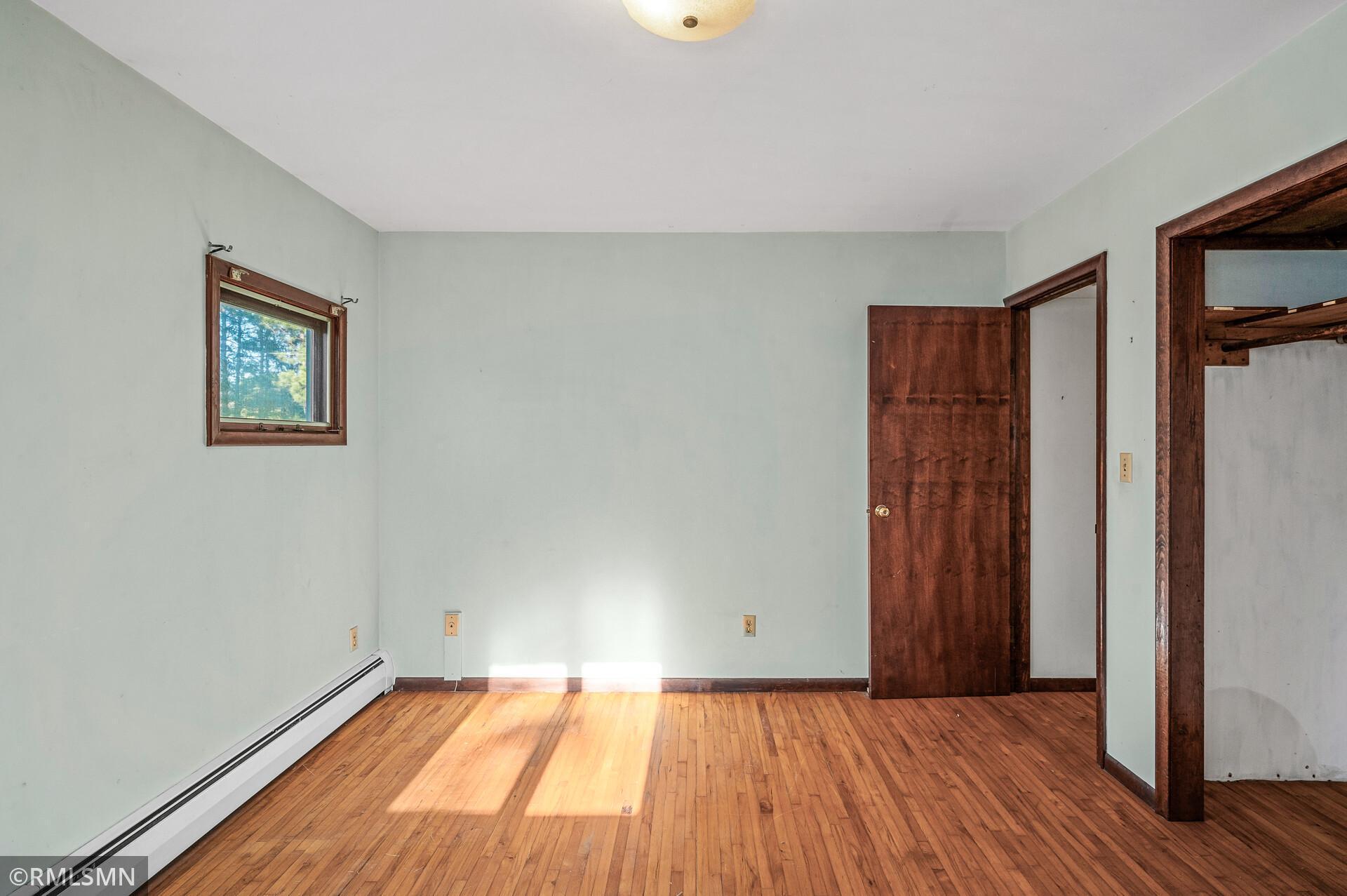 Empty room with hardwood floors, a small window, and an open closet doorway.