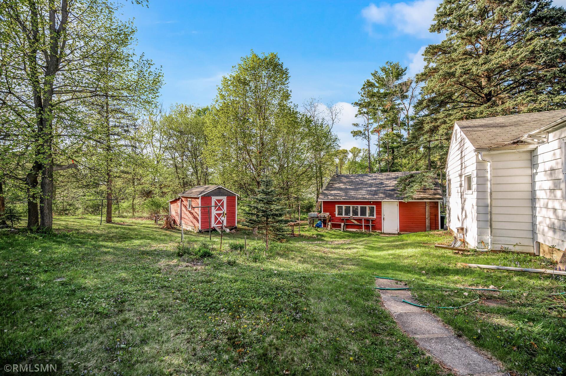 Tree-lined backyard with two red outbuildings, a white house, and a concrete walkway.