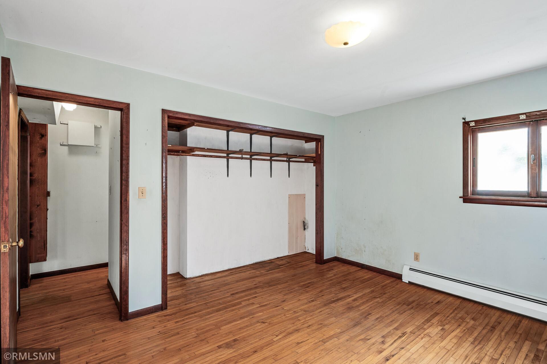 Vacant bedroom with hardwood floors, dark wood trim, and an open built-in closet.