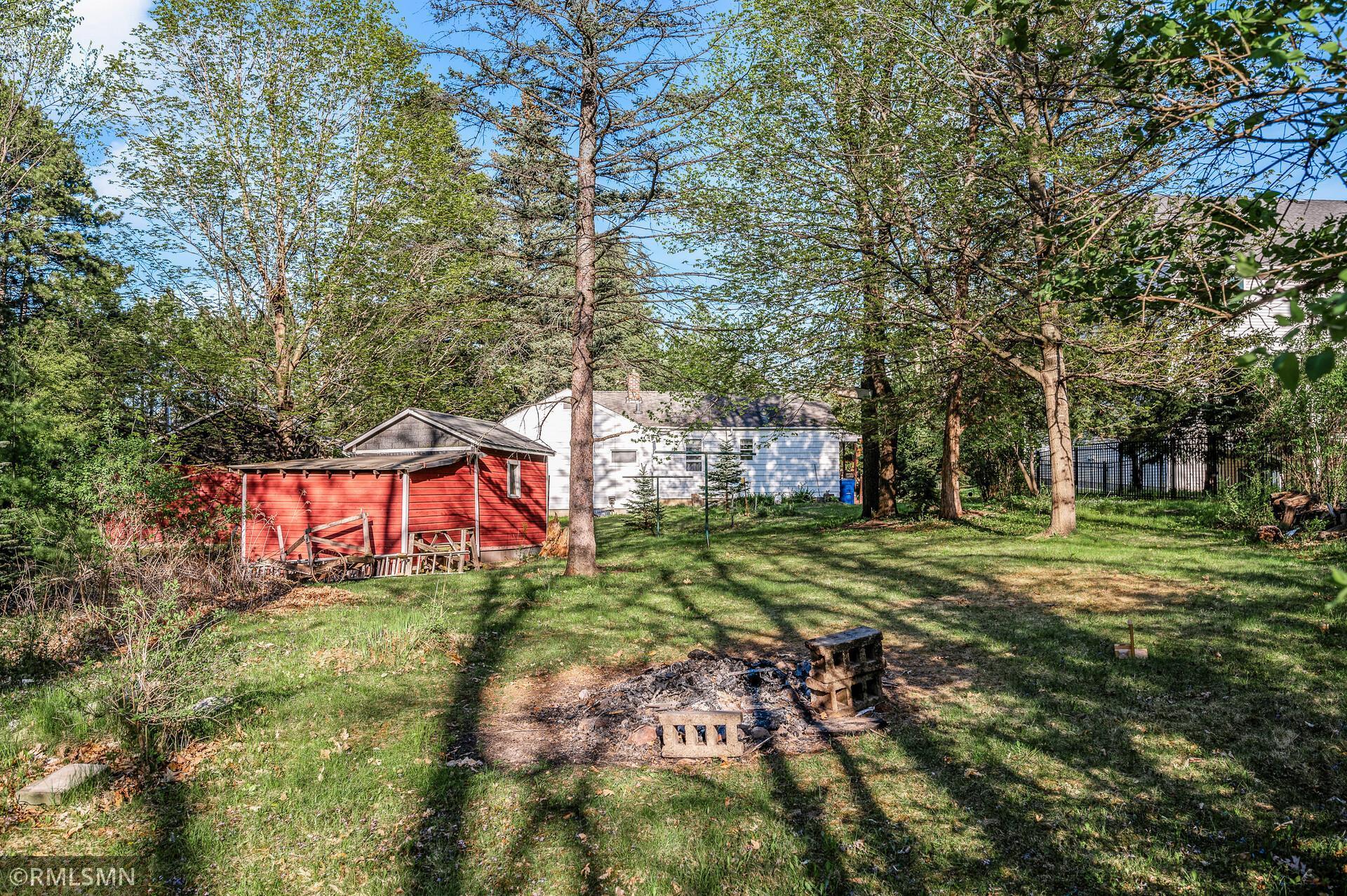 Wooded backyard with a white house, red shed, and stone fire pit.