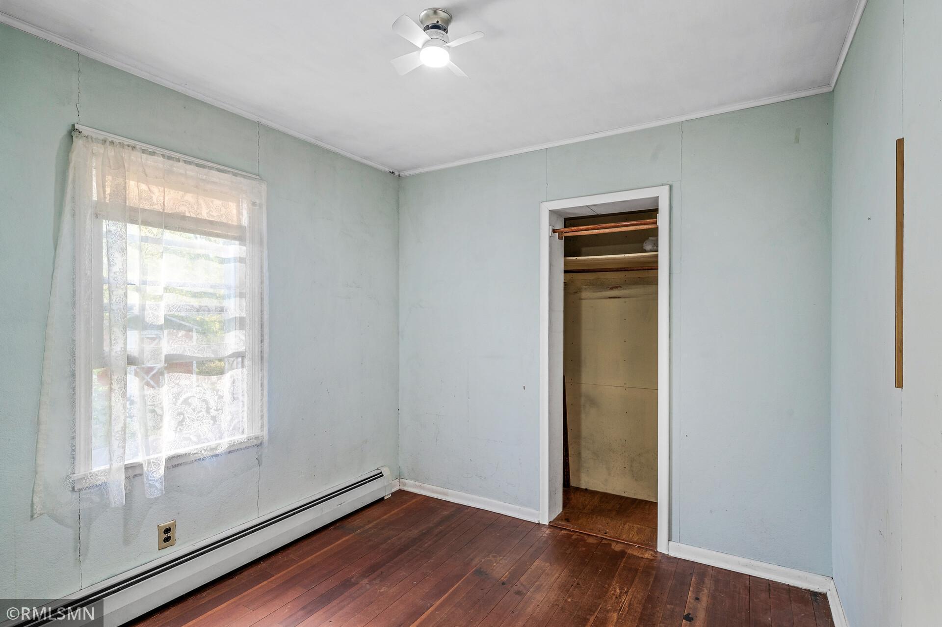 Unfurnished bedroom with lace curtains, hardwood flooring, and an open closet.