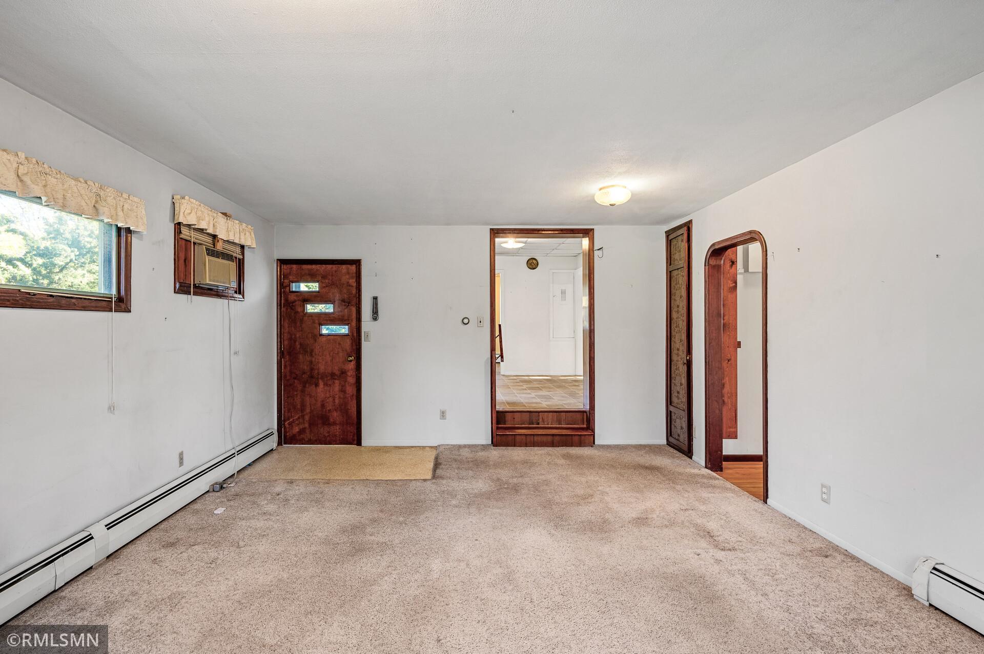 Empty living room with beige carpet, dark wood doors, and a window air conditioner.