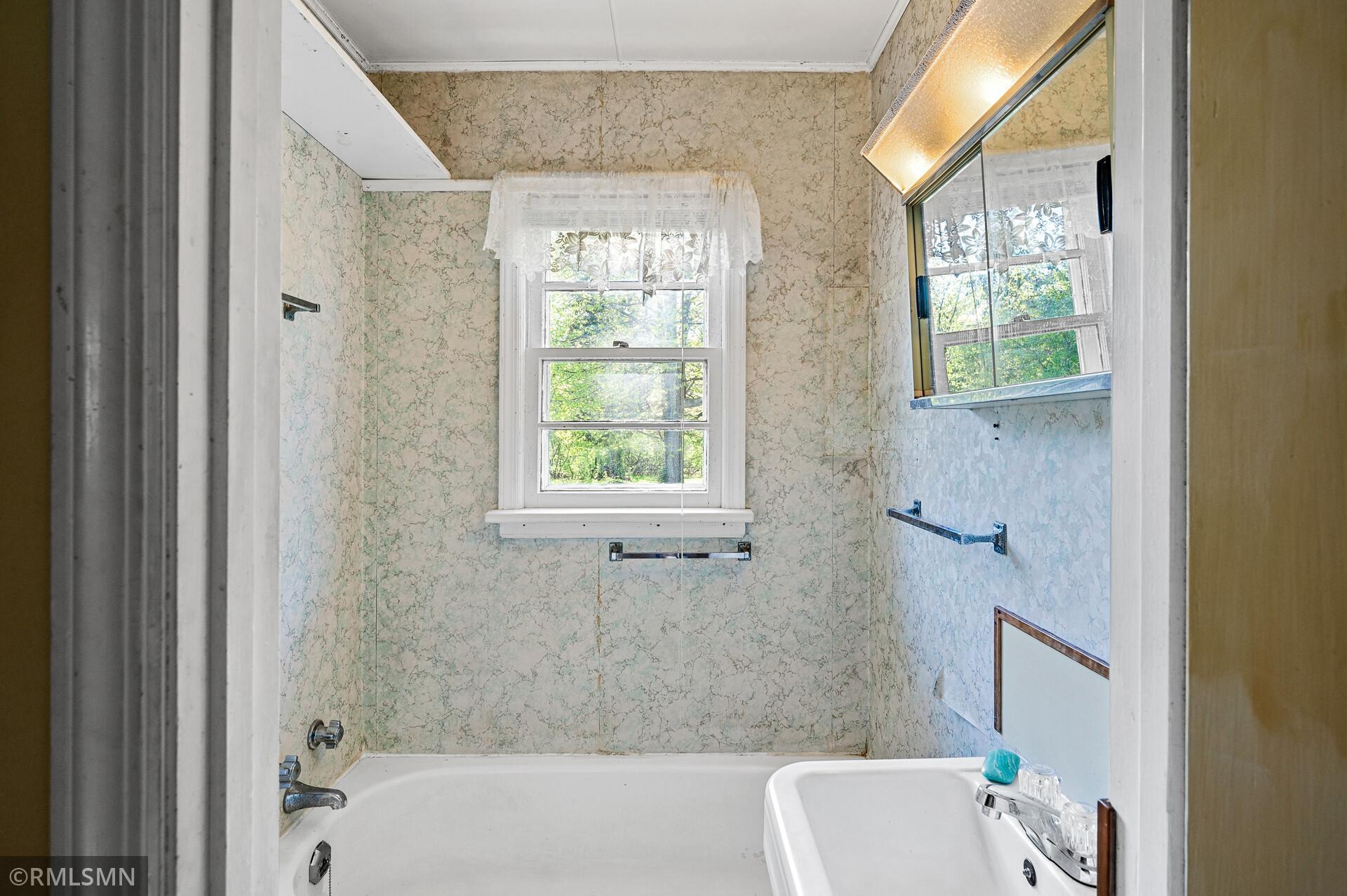Bathroom with a tub beneath a window and vintage-patterned wall panels.