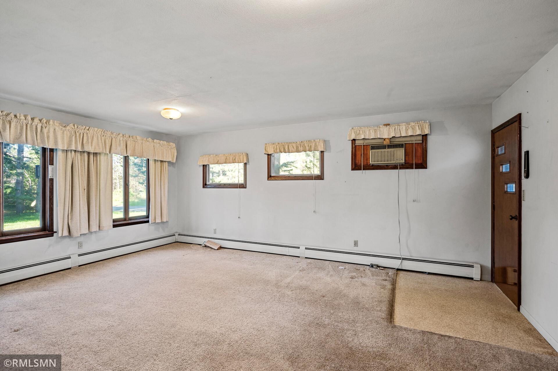 Empty living room with beige carpet, curtained windows, and a window air conditioner.