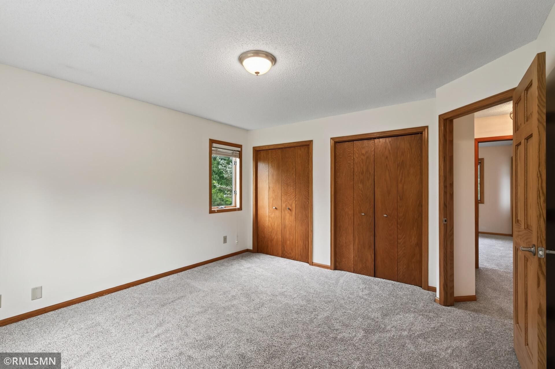 Empty bedroom with gray carpet, a small window, and two sets of wood closet doors.
