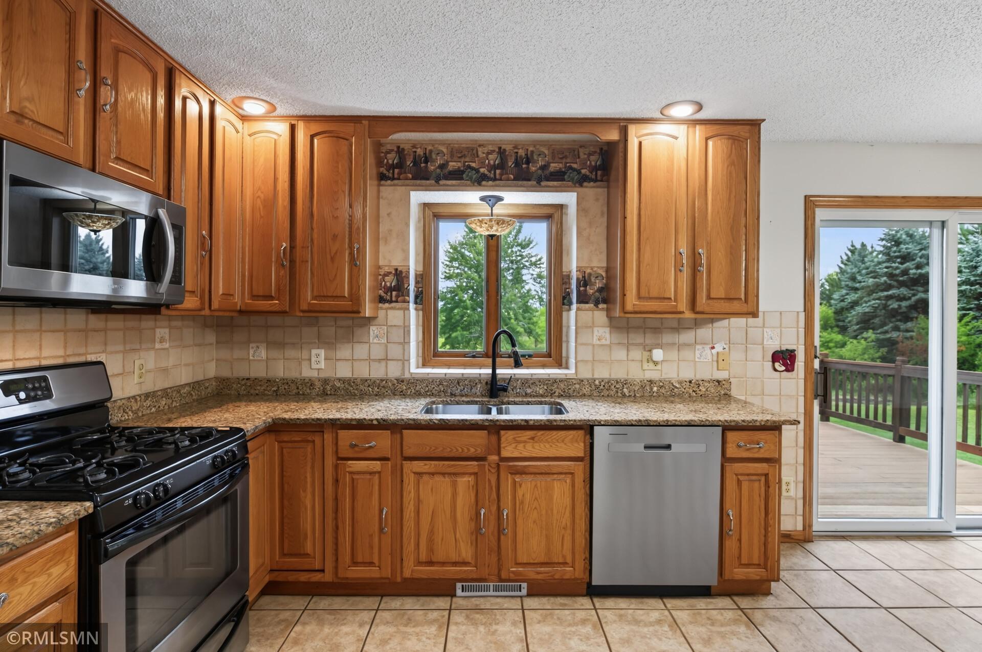 Kitchen with honey-toned wood cabinets, granite counters, stainless appliances, and a sink beneath a window.