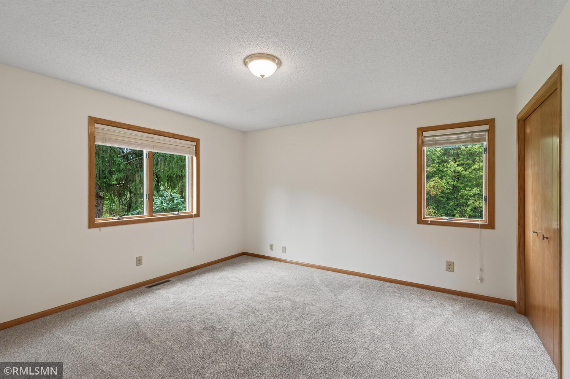 Vacant carpeted bedroom with wood-trimmed windows overlooking trees.