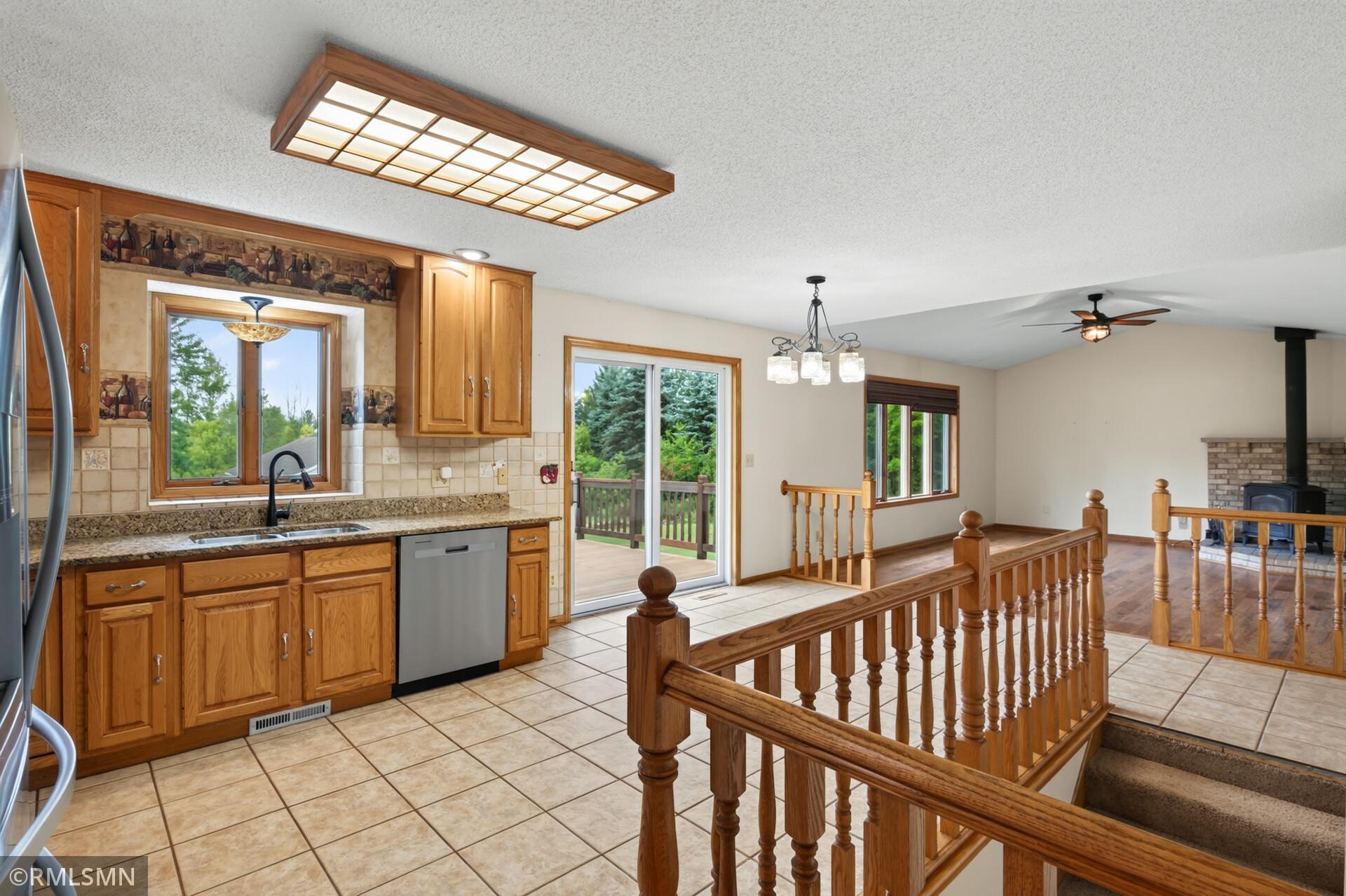 Kitchen with honey-colored wood cabinets, tiled floor, sliding deck door, and railing overlooking the stairs.