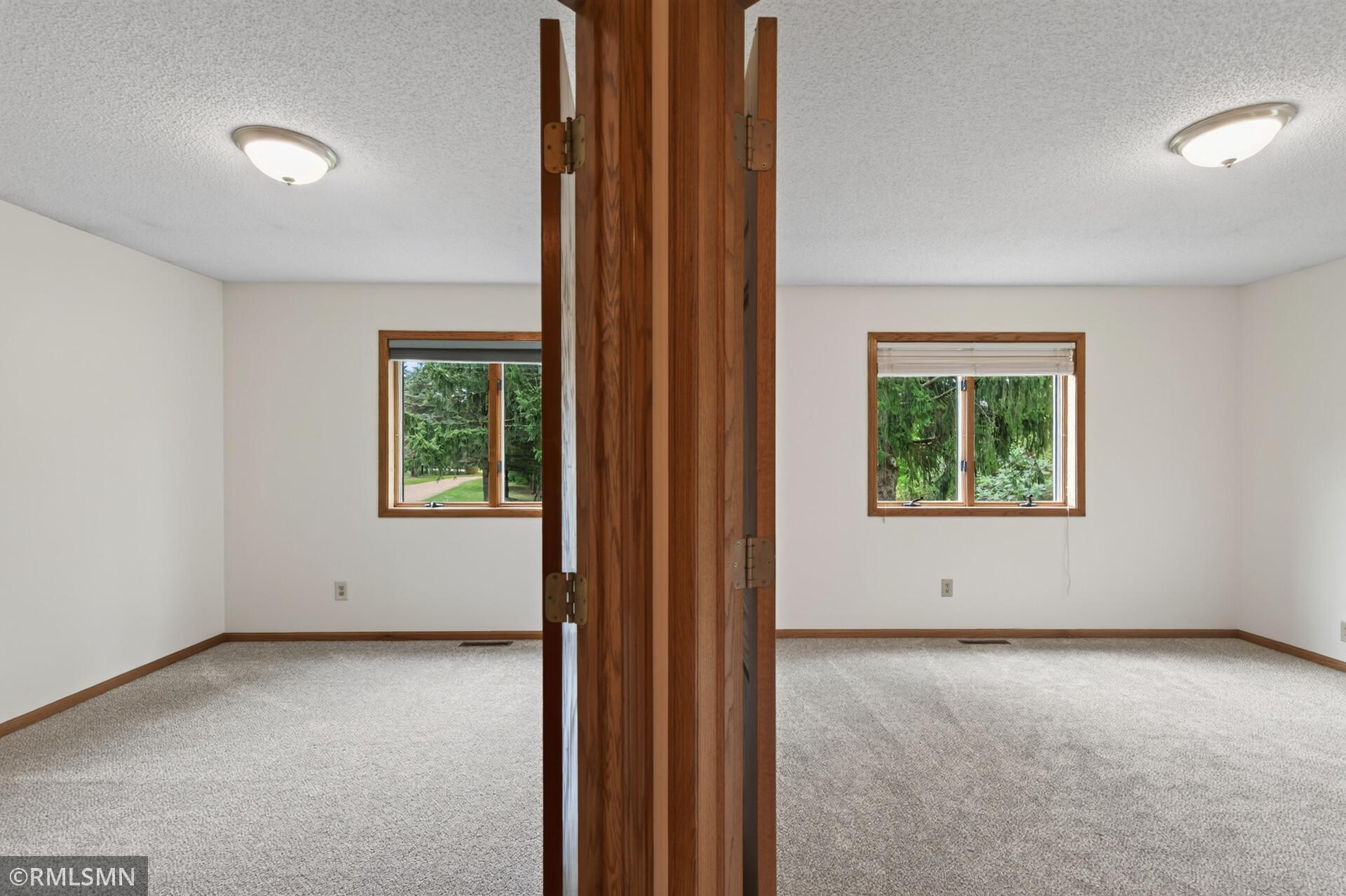 Two adjoining carpeted rooms divided by a tall wooden folding partition, with windows overlooking trees.