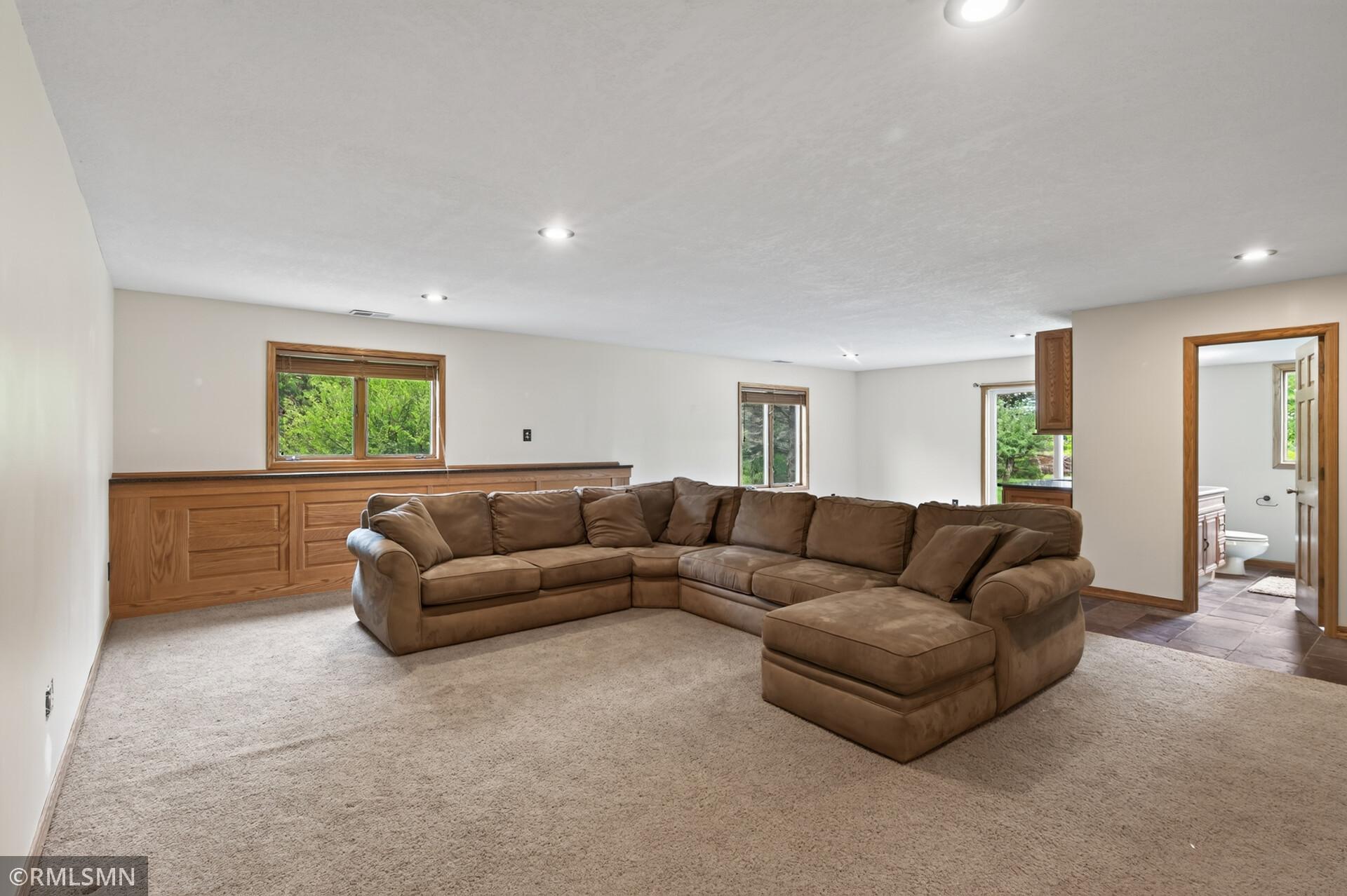 Living room with a large brown sectional, built-in wood cabinetry, and an adjoining bathroom doorway.
