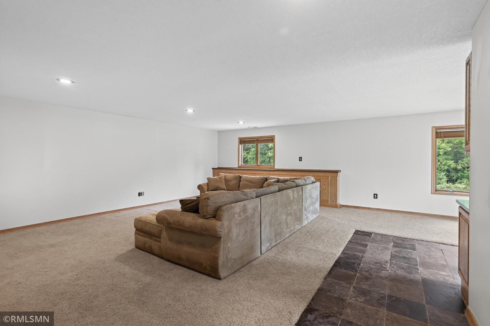 Living room with a large brown sectional, beige carpet, and a dark tiled floor area.
