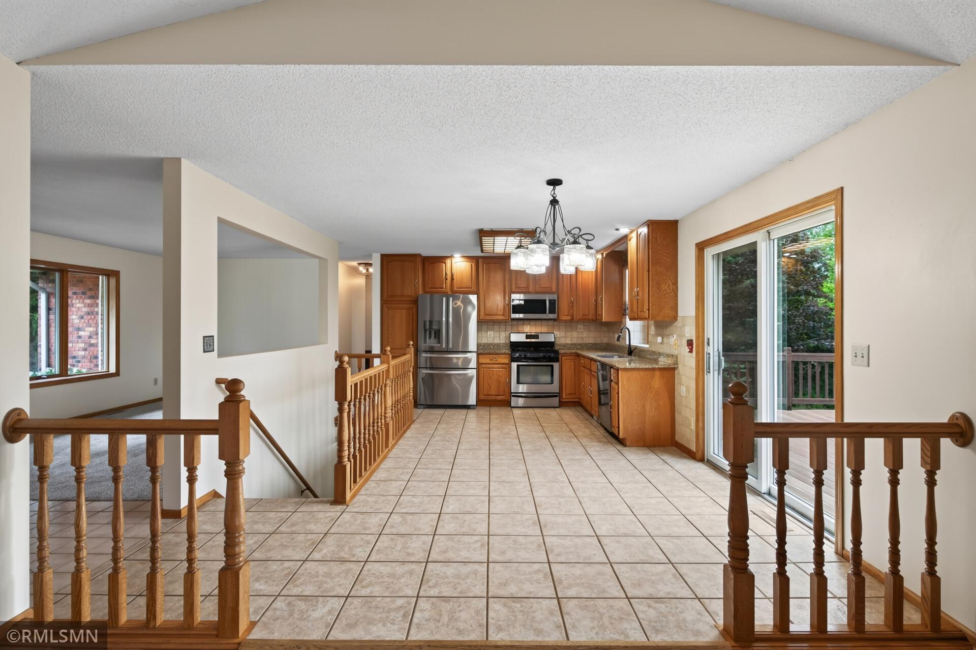Kitchen with wood cabinetry, stainless steel appliances, tiled floors, and sliding doors to a deck.